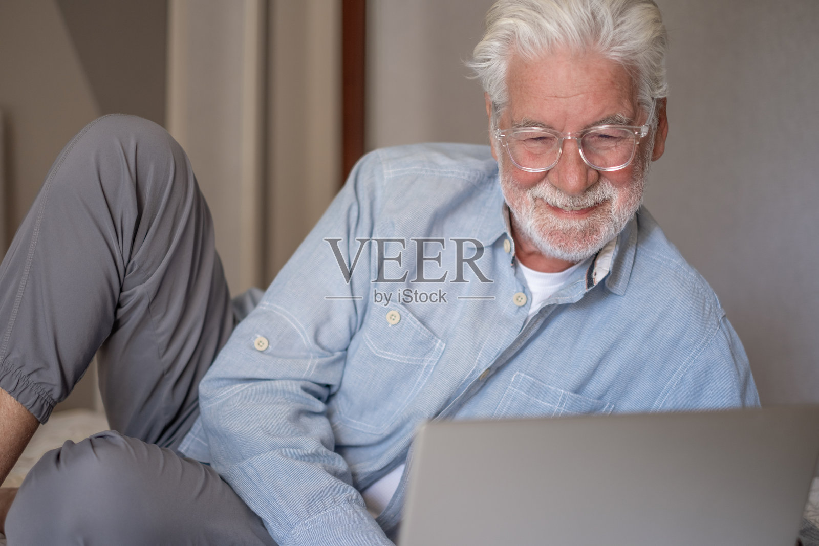 微笑的英俊白人老年男子,戴着眼镜,躺在床上使用电脑,退休老人正在用笔记本浏览互联网照片摄影图片