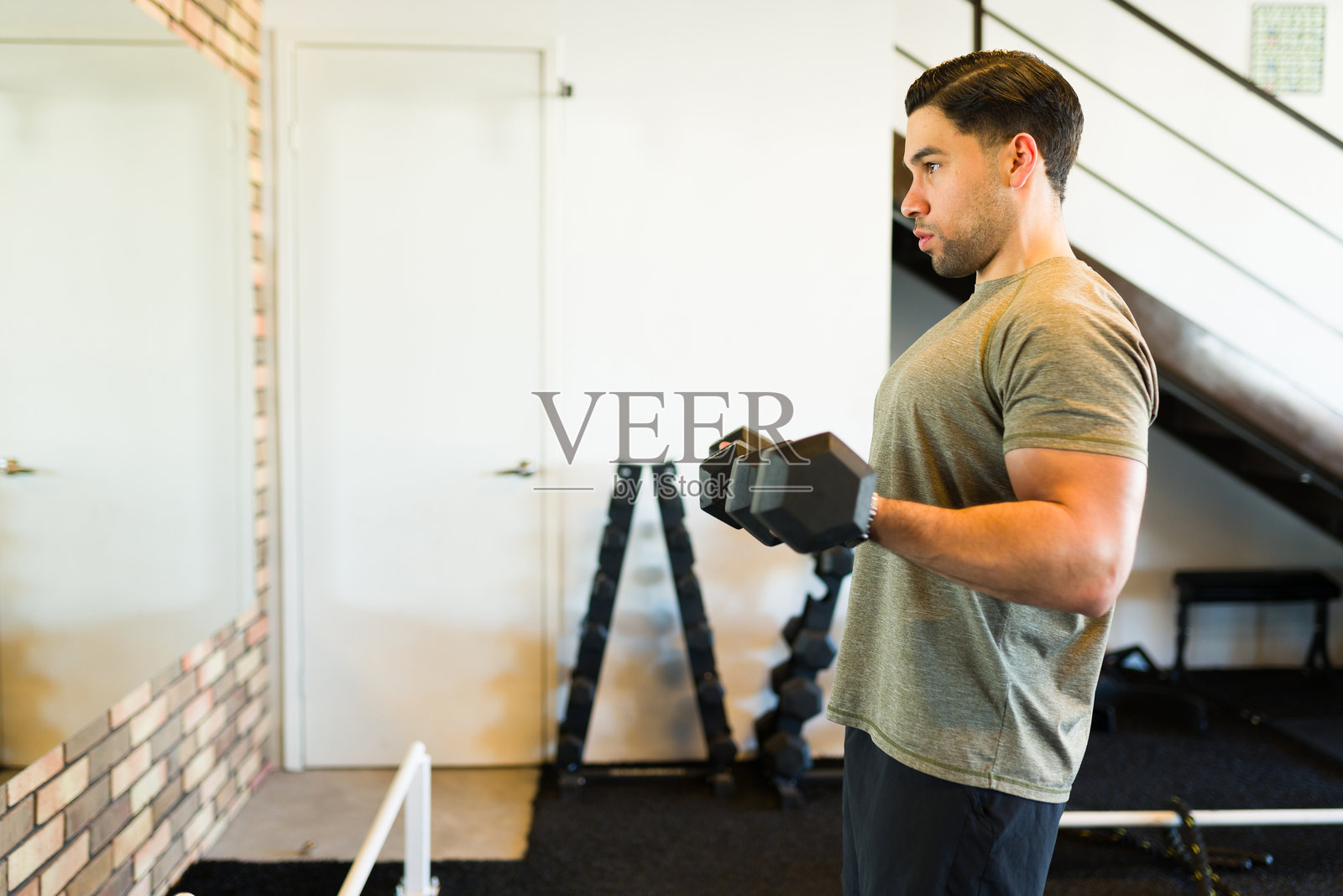 肌肉发达的男性在现代健身房中进行哑铃举重,展现出强烈的健身训练。照片摄影图片