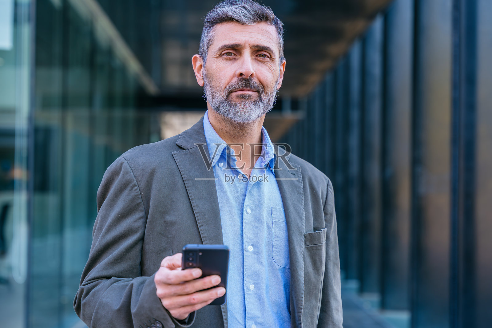 自信的商人在户外使用智能手机并看向镜头。照片摄影图片