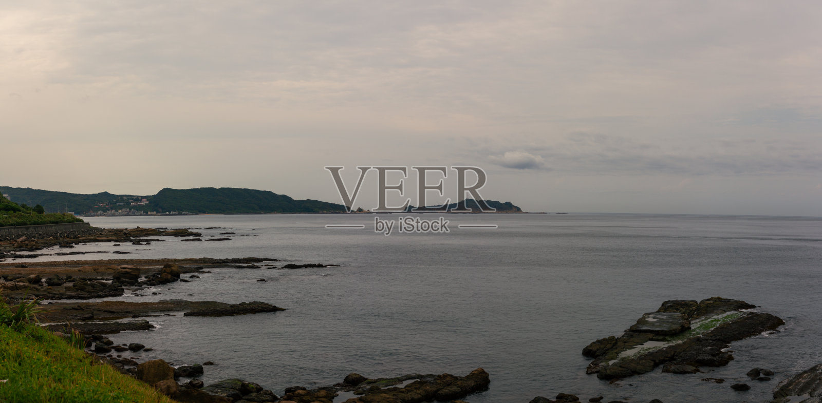 台湾柔和阴云下的宁静海岸景观,岩石海岸与绿色山丘相映成趣照片摄影图片