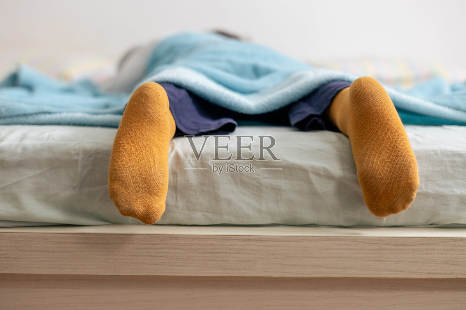 孩子安静地躺在床上,穿着黄色袜子,盖着蓝色的毯子。照片摄影图片