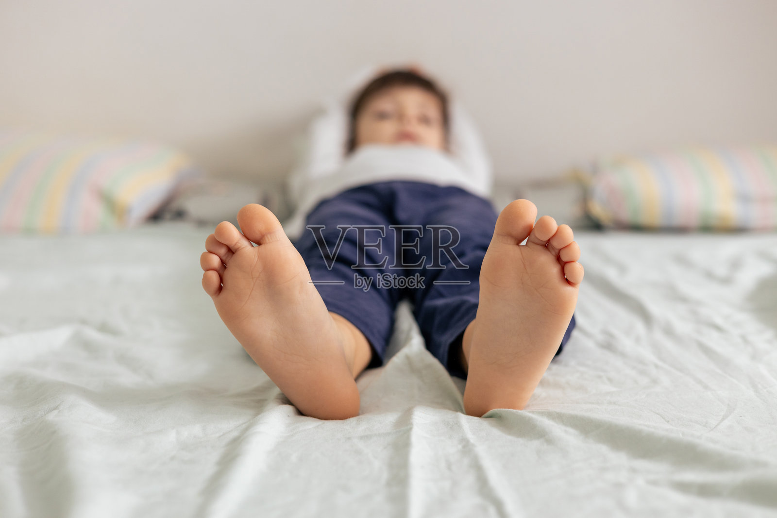 孩子躺在床上,脚朝向镜头。照片摄影图片