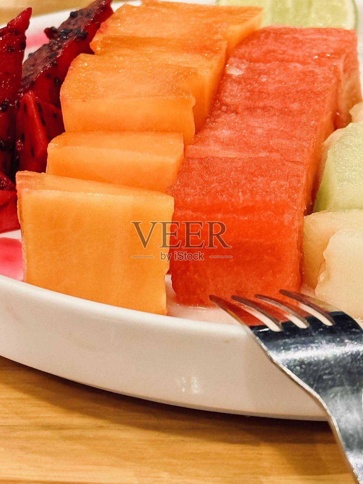 新鲜切片水果放在盘子里,旁边有叉子照片摄影图片