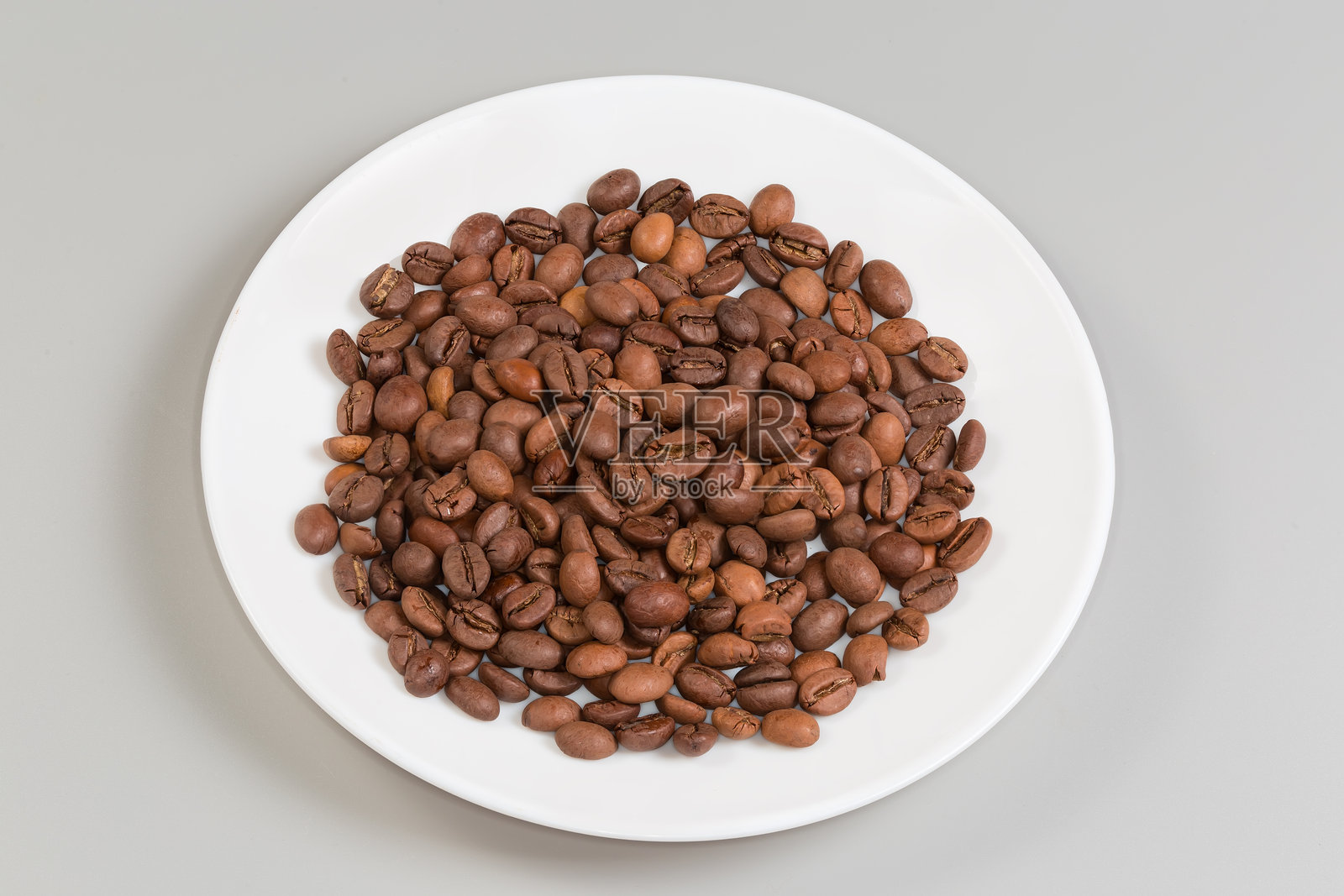白盘子上的烘焙咖啡豆,背景为灰色照片摄影图片