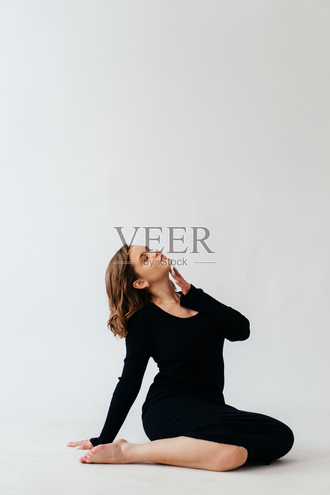 一位自信的年轻女性穿着黑色罗纹中长裙,在简约的白色背景前优雅地摆姿势,展现出优雅与风格。照片摄影图片