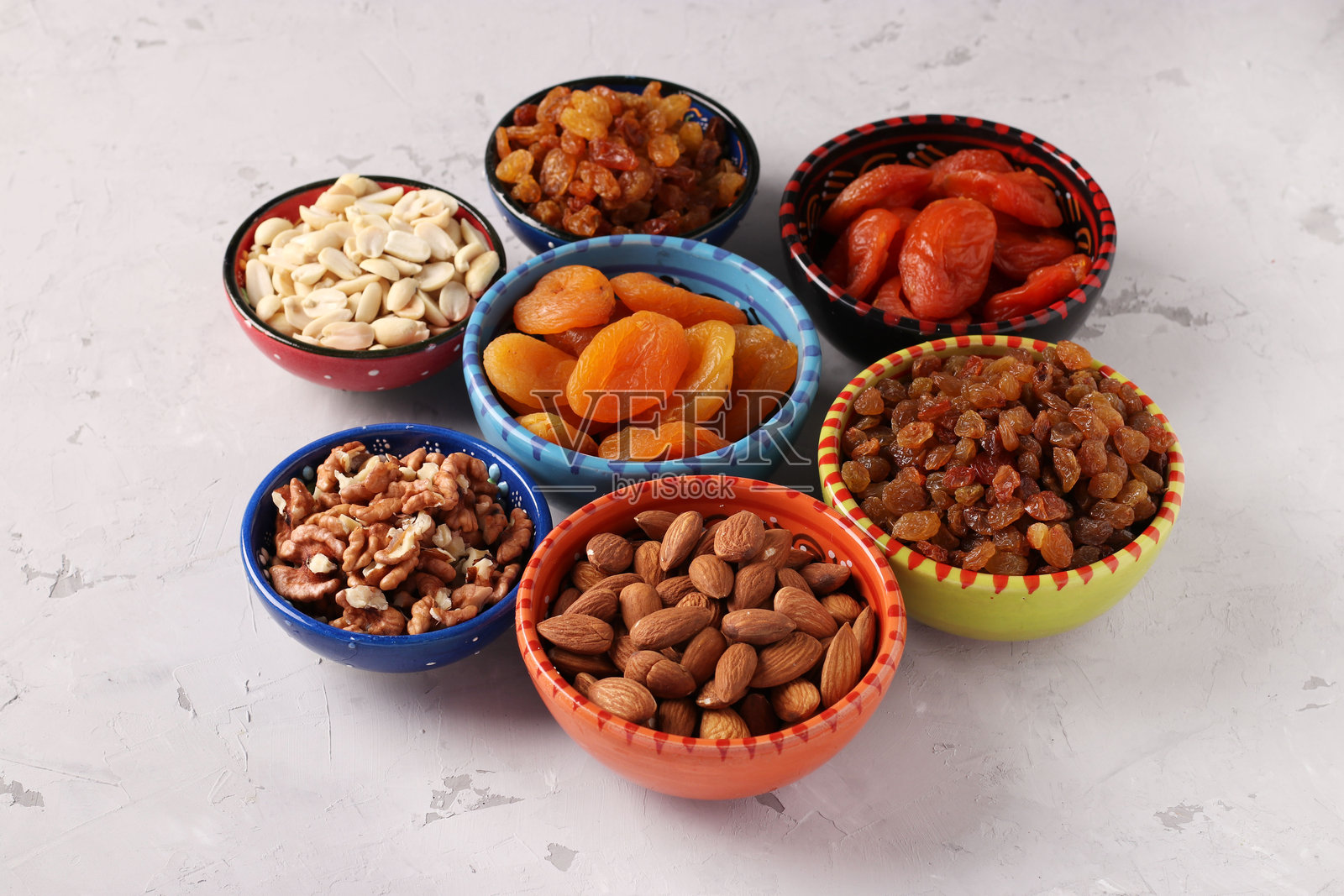 灰色混凝土背景上的碗里装有干杏、葡萄干、花生、杏仁和核桃,特写镜头照片摄影图片