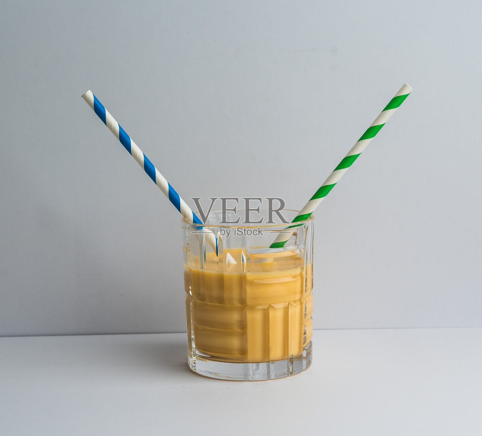 清新的芒果冰沙盛在玻璃杯中,配有五彩缤纷的吸管,背景简约。照片摄影图片