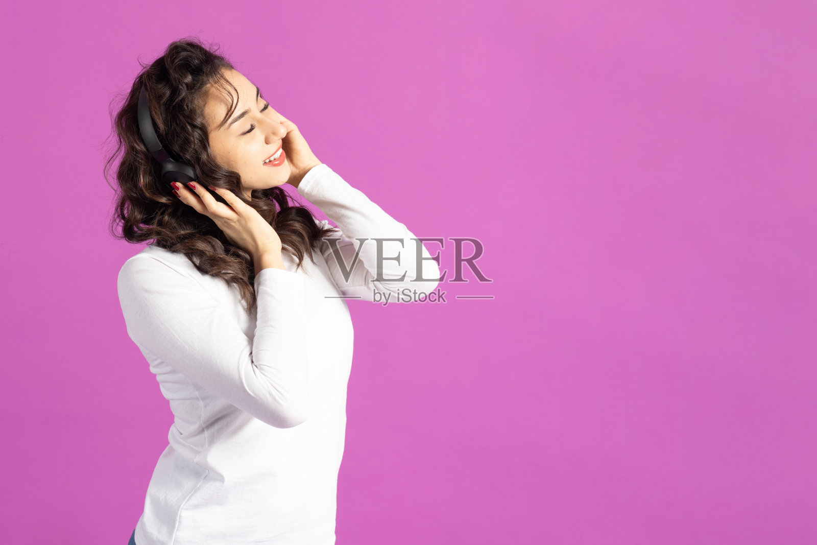 戴着耳机的女性,背景为粉色照片摄影图片