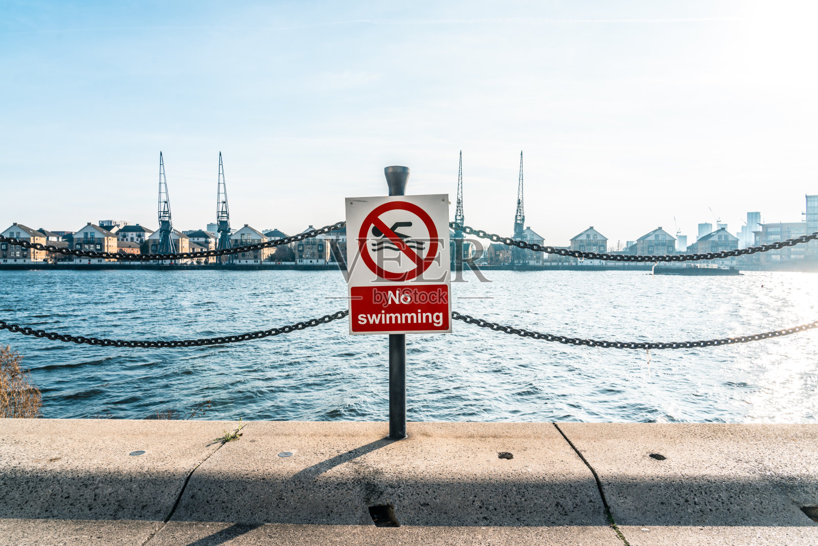 伦敦码头区的禁止游泳标志,背景有起重机。照片摄影图片