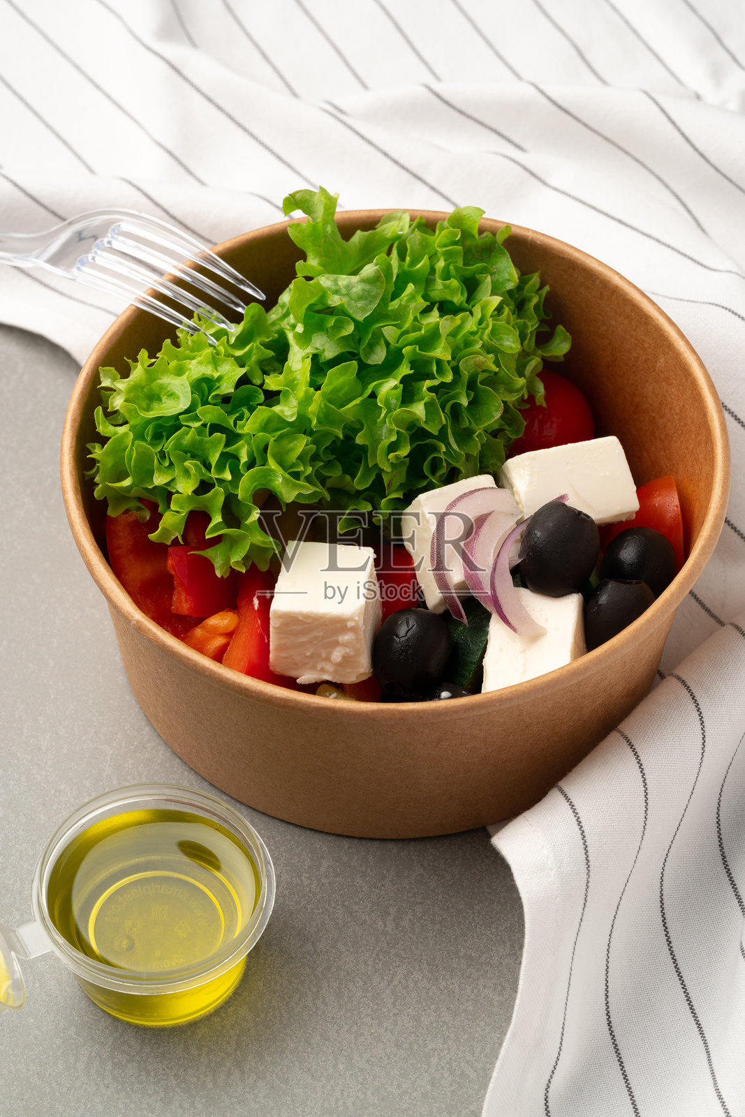 新鲜沙拉,配有生菜、西红柿、橄榄和奶酪,摆放在灰色桌子上,准备享用健康餐。照片摄影图片