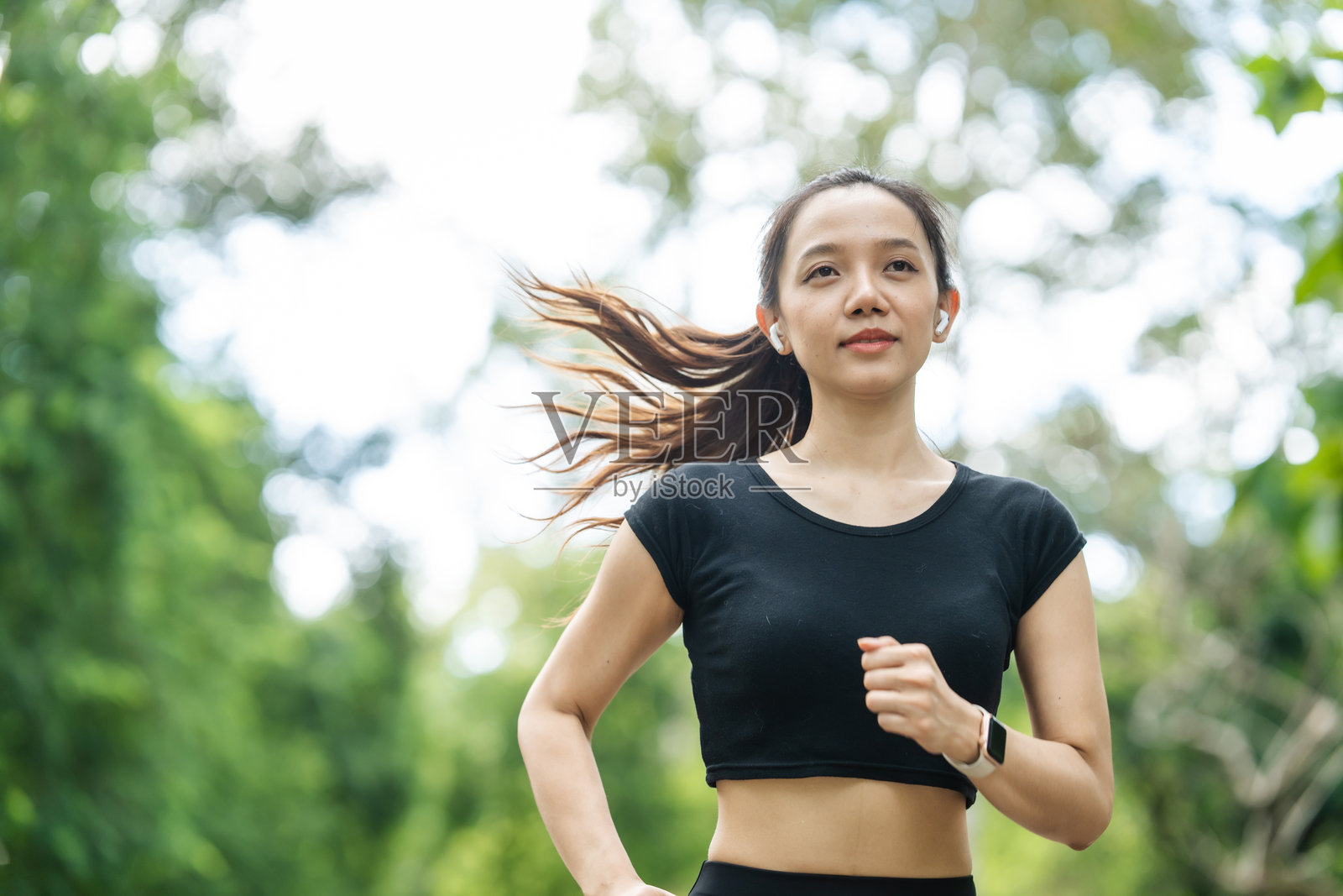 一位穿着运动服的女性在公园里跑步,享受新鲜空气,参与户外活动以保持健康的生活方式,增强心血管健康,感到快乐和充满活力。照片摄影图片