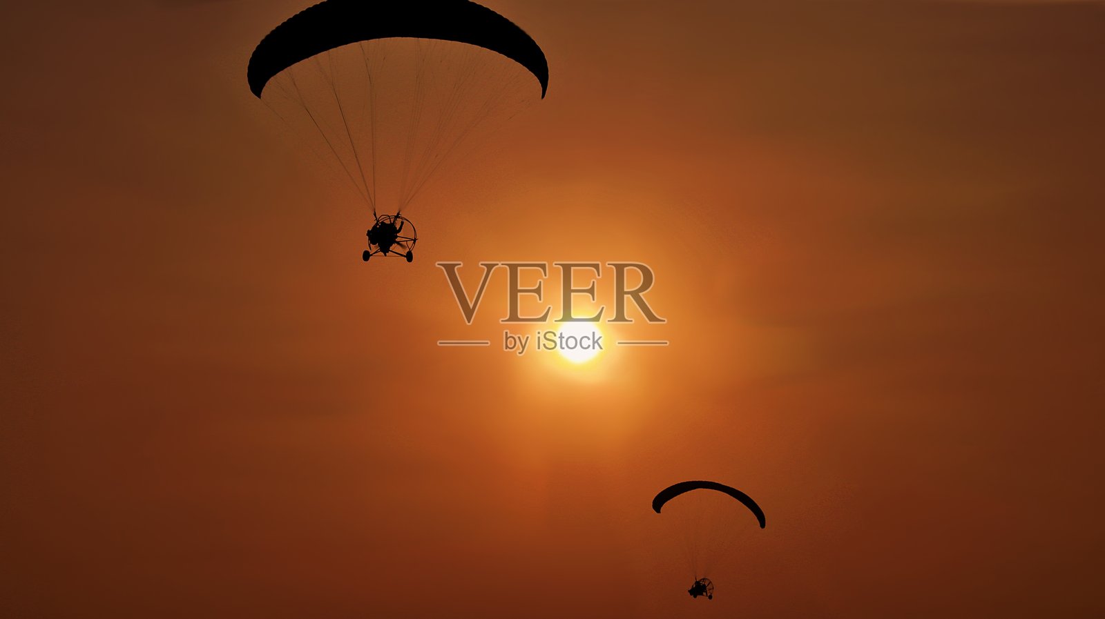 日落时分,低角度拍摄的人在天空中滑翔伞飞行照片摄影图片