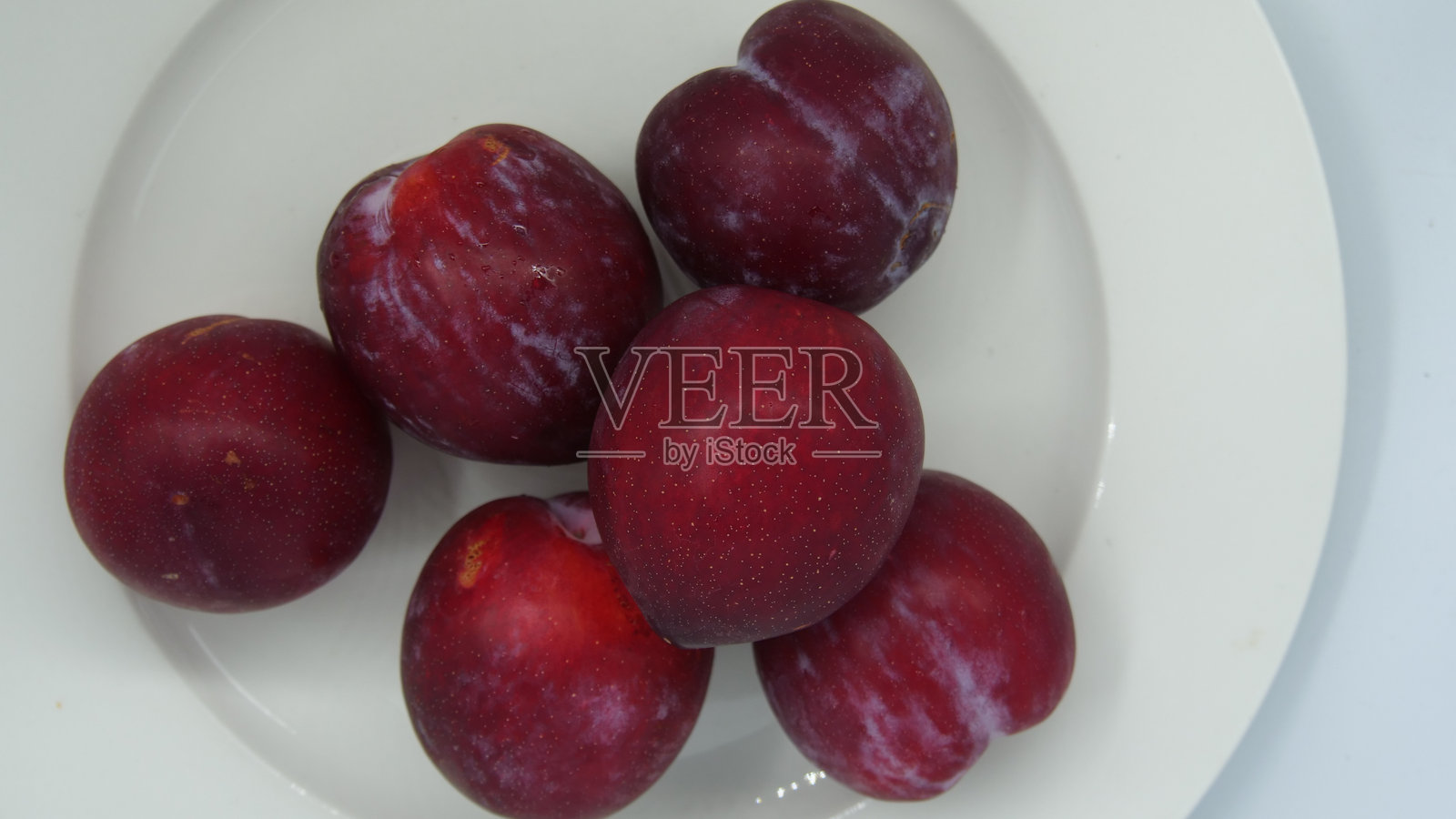 从上方俯视深红色李子放在白色盘子上照片摄影图片