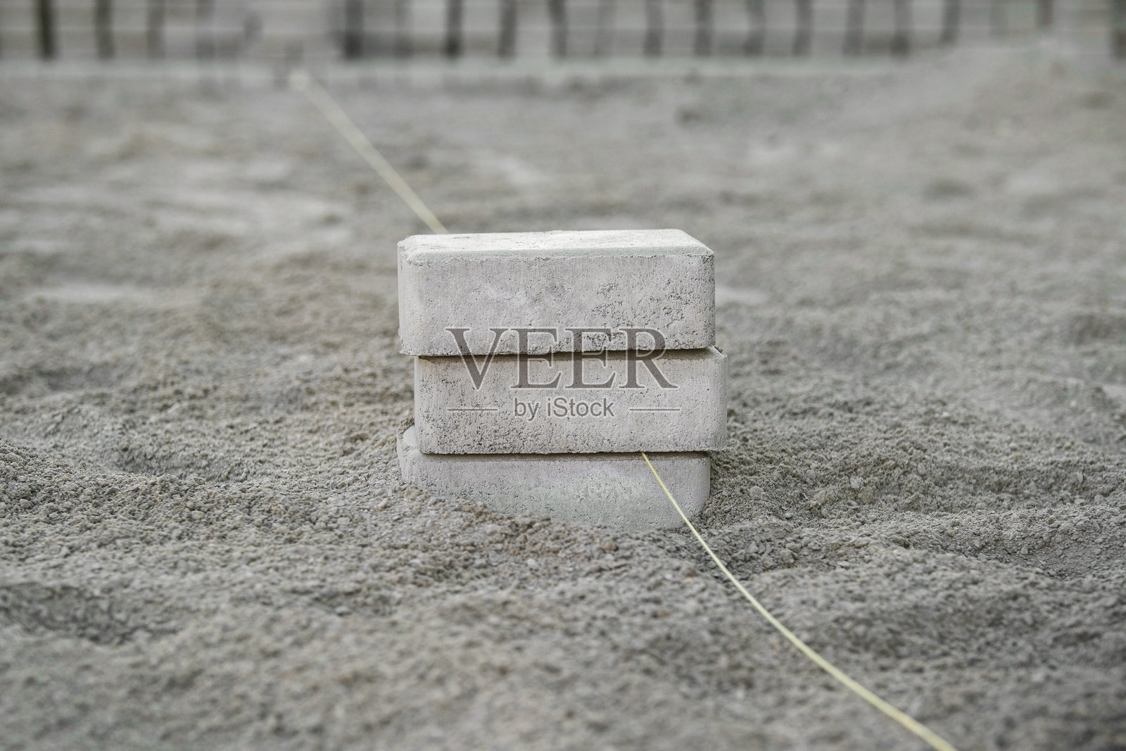 混凝土块锚固在沙质地形中,支撑着用于建筑或园艺工作的测量线。照片摄影图片