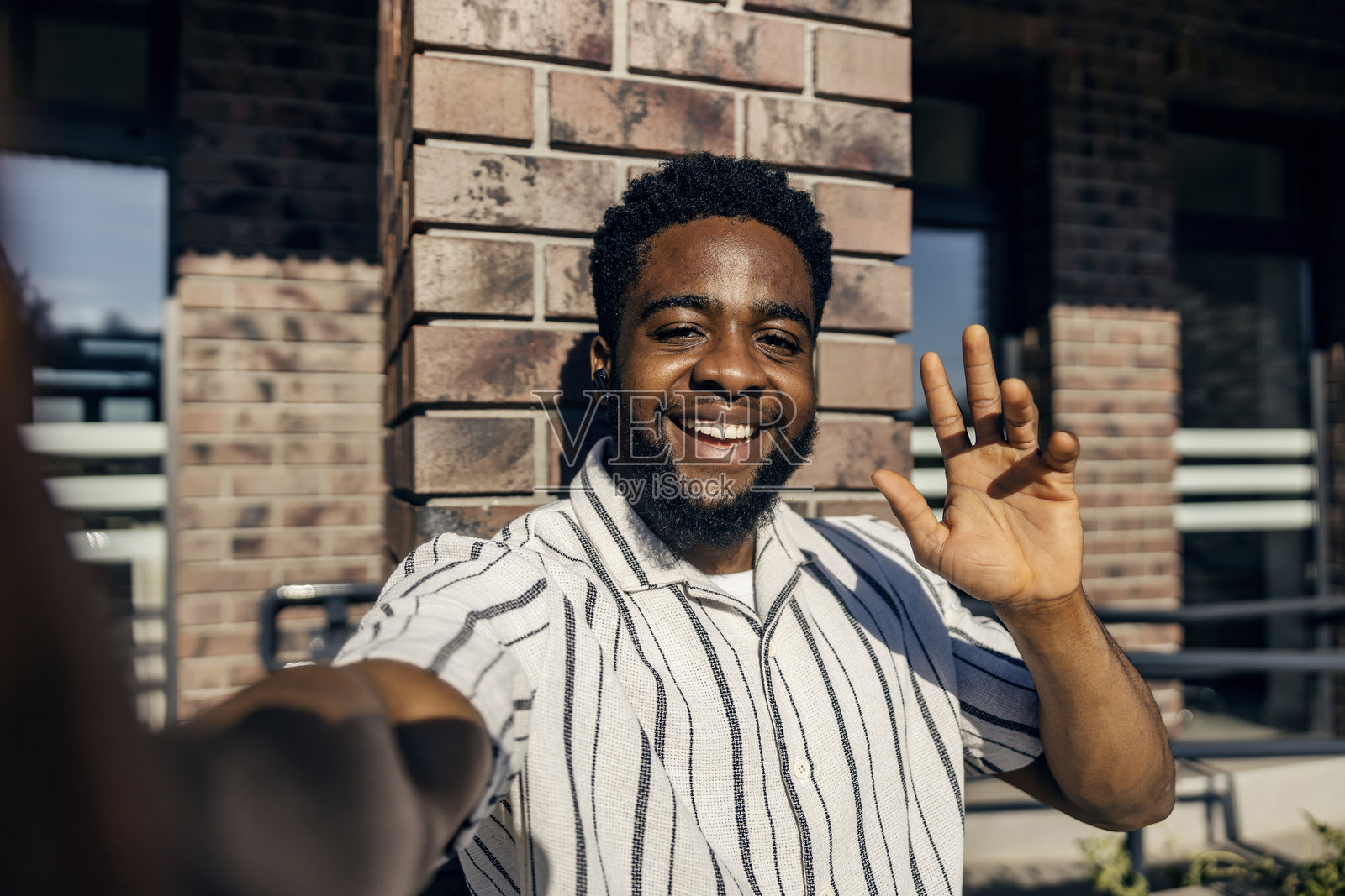 年轻的黑人乘客在公交车站站着,正在进行视频通话并向镜头挥手。照片摄影图片