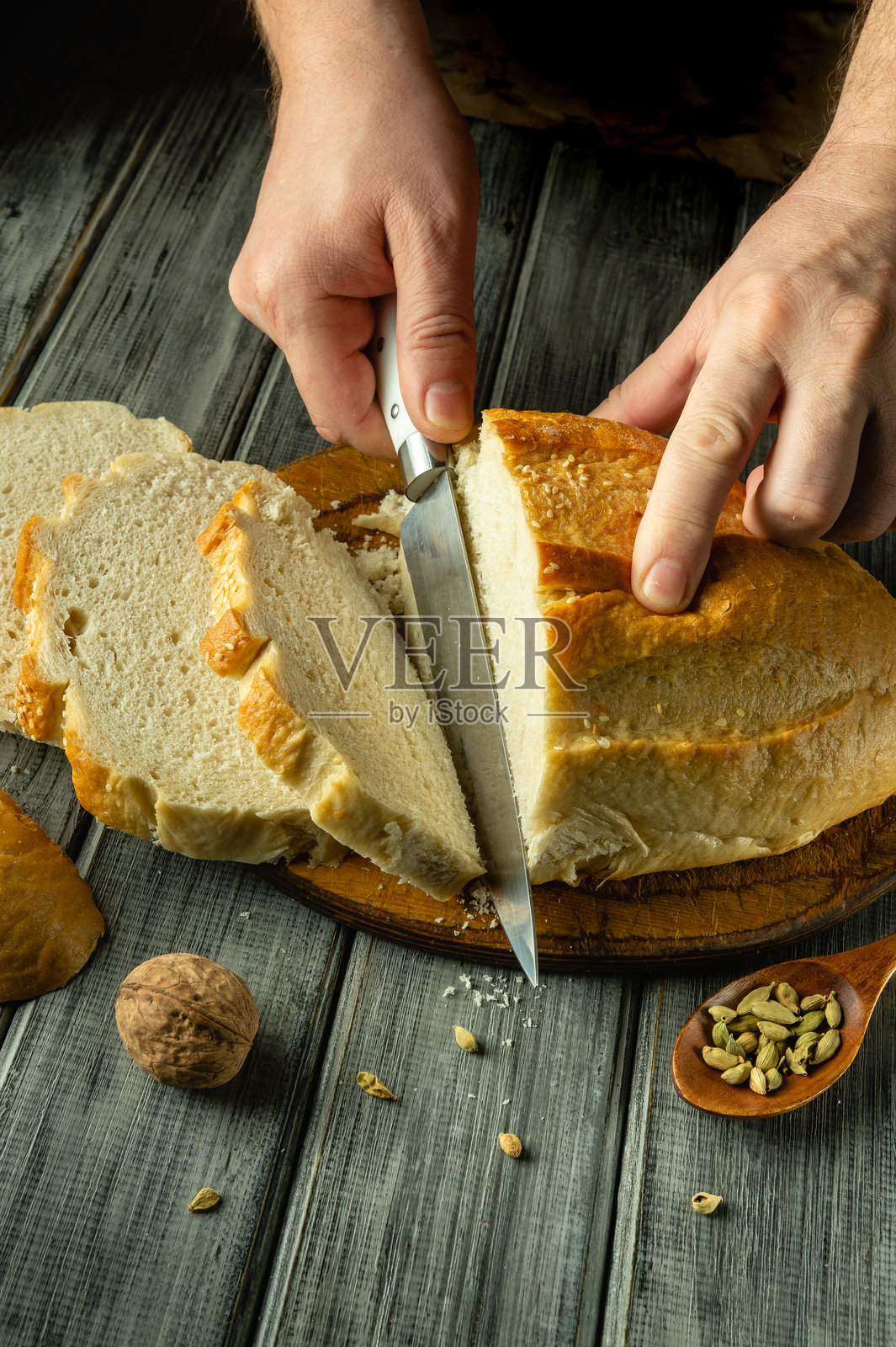 金黄色的面包静静地放在木板上,熟练的手切割着它柔软的内部。温暖的厨房氛围增添了烘焙和分享的快乐。照片摄影图片