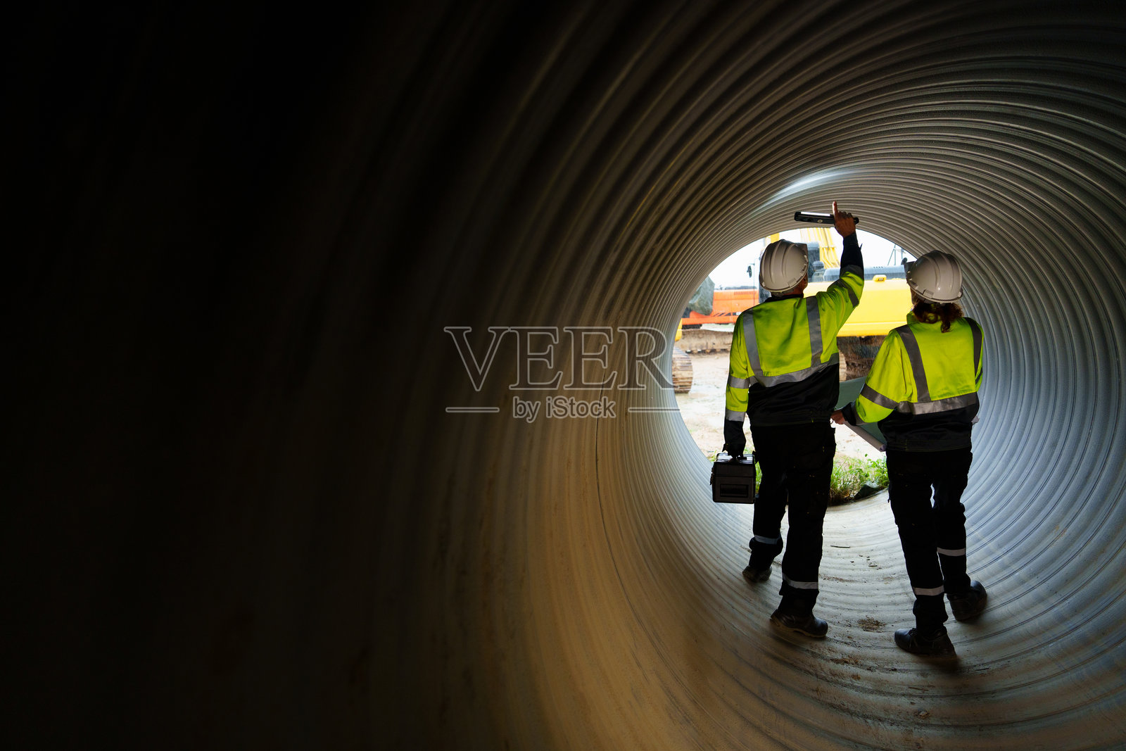 男女工程师在大型钢管内工作。工人们正在建造管道,以便在工业厂房中运输石油、天然气和燃料。照片摄影图片