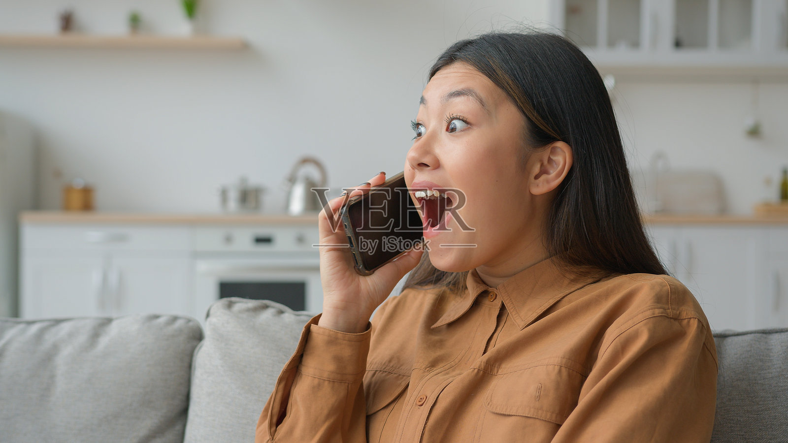 兴奋的亚洲女商人在厨房里打电话,听到好消息感到震惊和惊喜,韩国女孩在手机上愉快地讨论新闻,欢笑交谈,庆祝成功。照片摄影图片