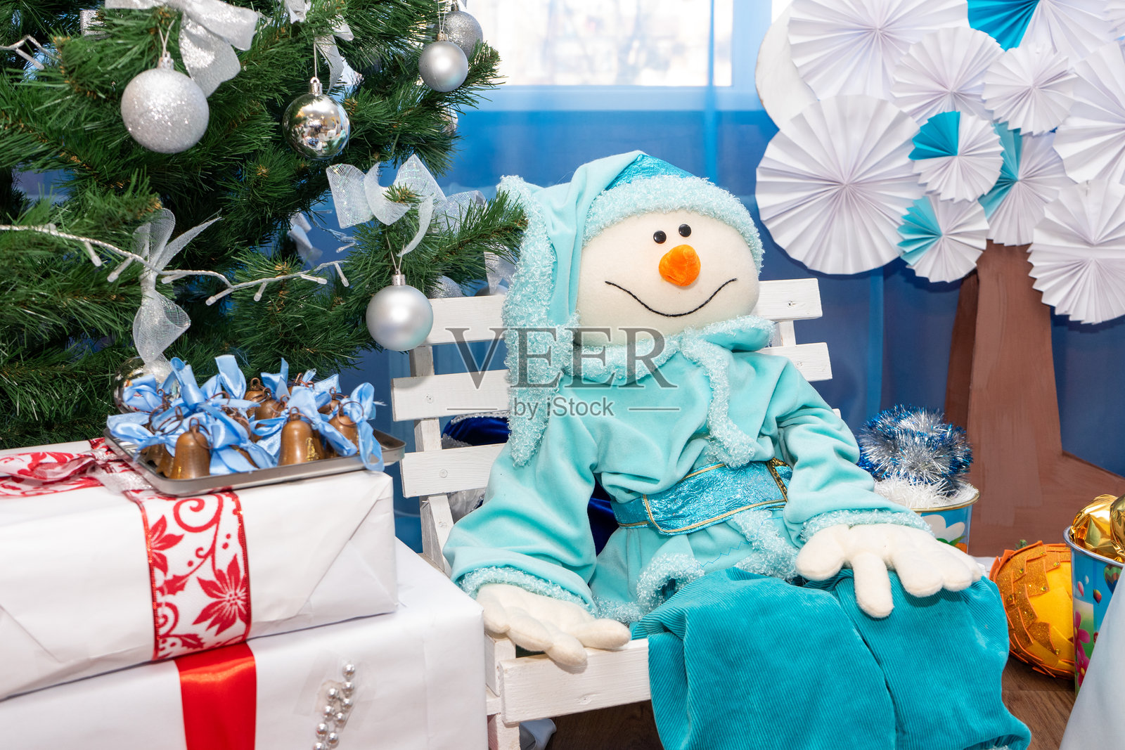 一个快乐的雪人坐在圣诞树下的白色长椅上照片摄影图片