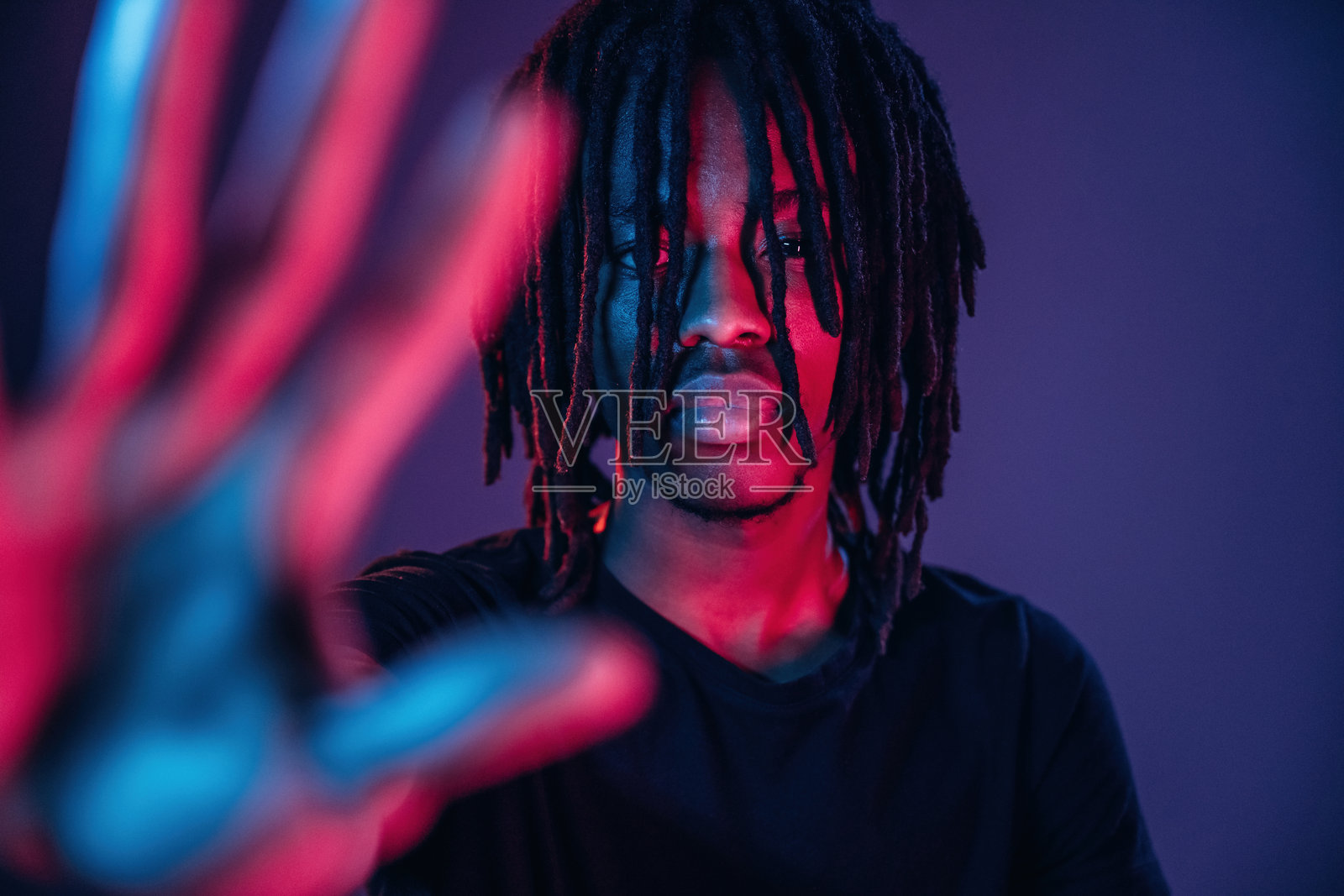 非裔美国男性在霓虹灯照明的摄影棚中做出停止手势。照片摄影图片