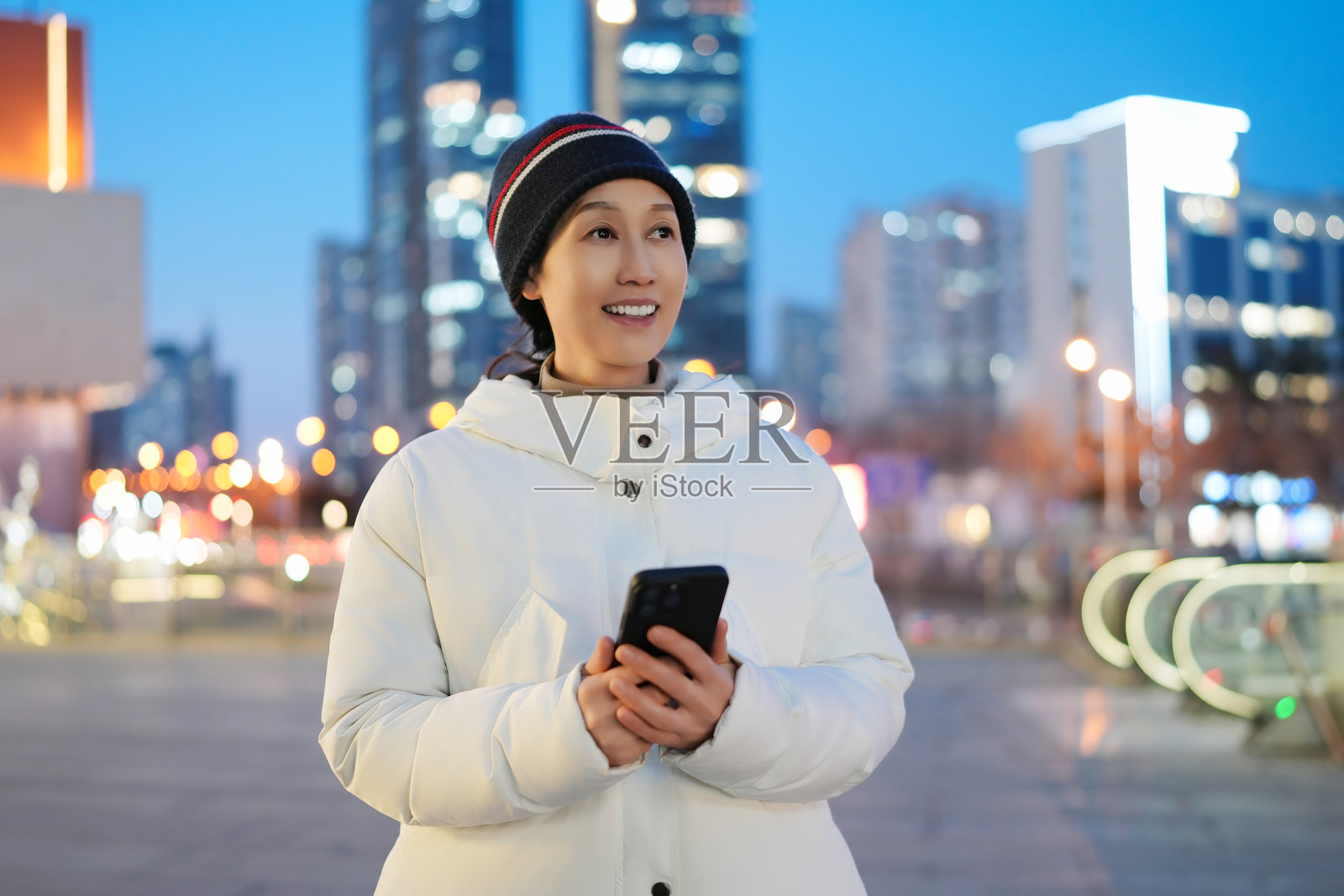 黄昏时分,城市环境中微笑的年轻女性手持智能手机照片摄影图片