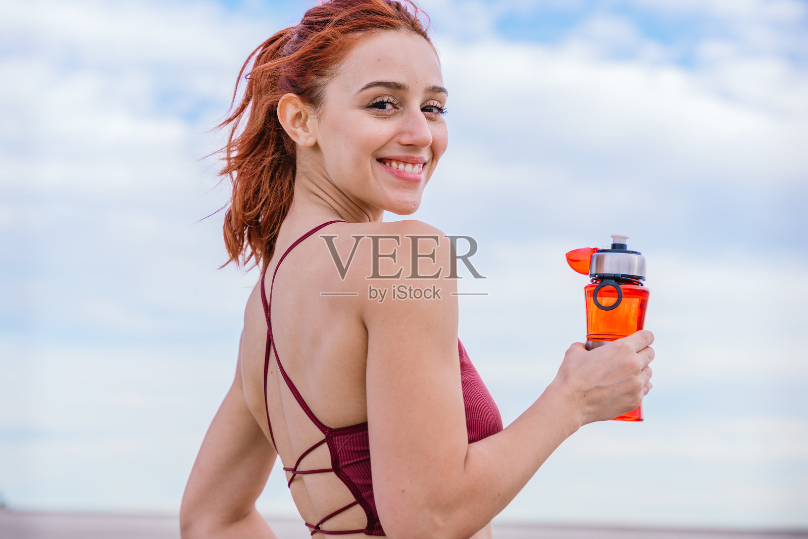 微笑的运动女性在蓝天之下户外手持水瓶照片摄影图片