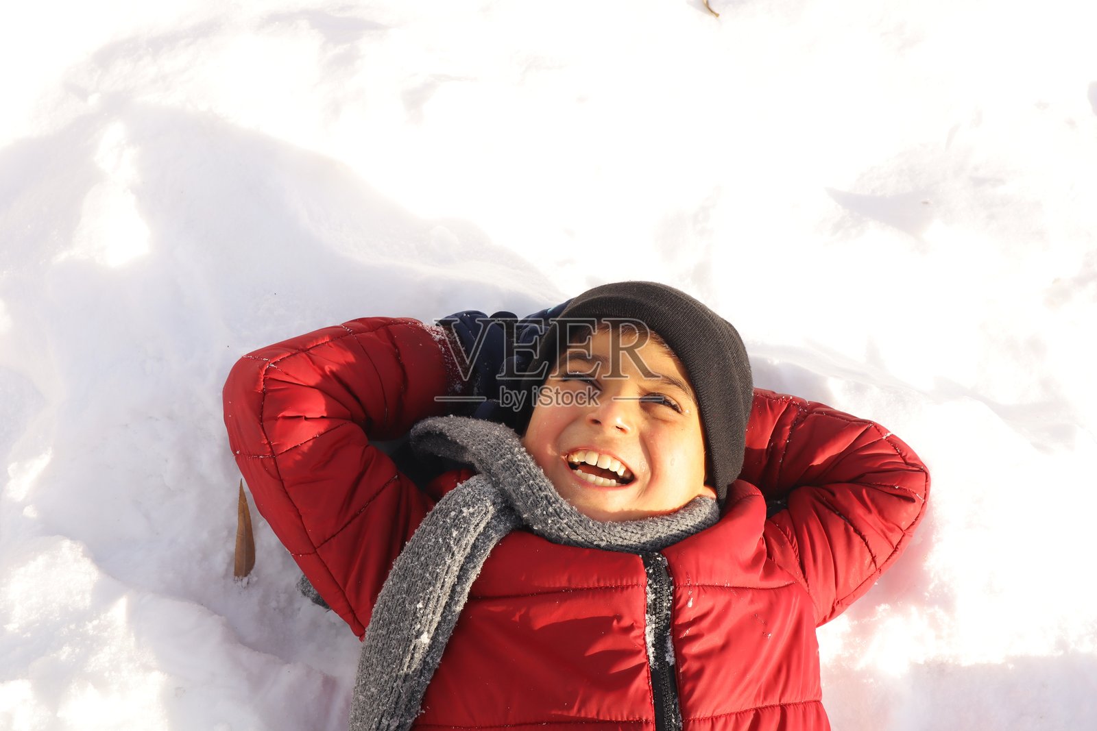 年轻男孩快乐地躺在雪地上,脸上挂着灿烂的笑容,尽情享受这一刻。照片摄影图片