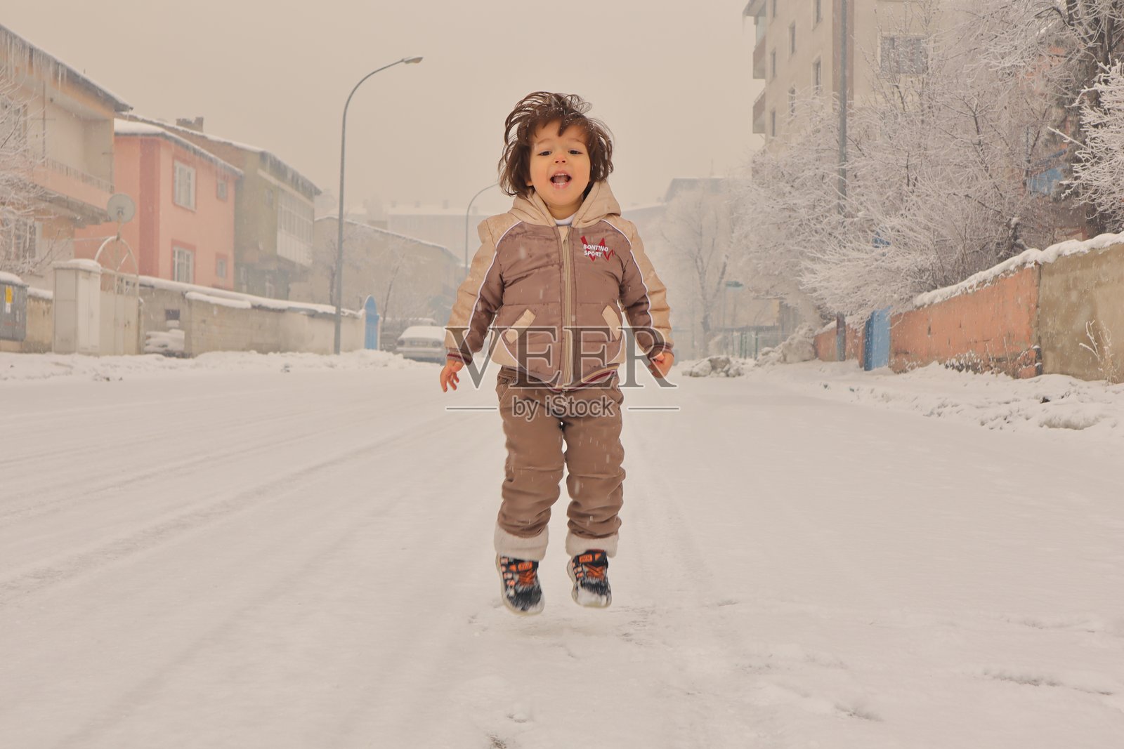 快乐的小孩在雪花轻轻飘落的环境中兴奋地跳跃,捕捉到体验降雪的纯粹喜悦和惊奇。一个充满幸福和活力的温馨冬季场景。照片摄影图片