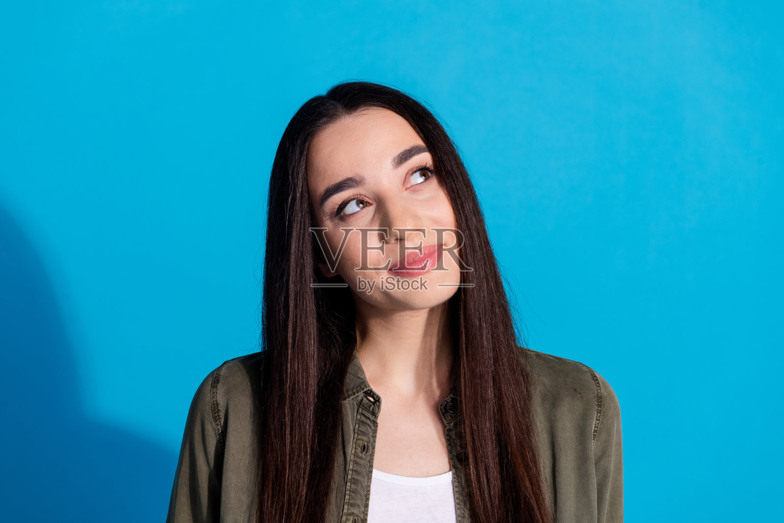 年轻的棕发女性在蓝色背景前摆姿势,展示休闲时尚和迷人的表情照片摄影图片