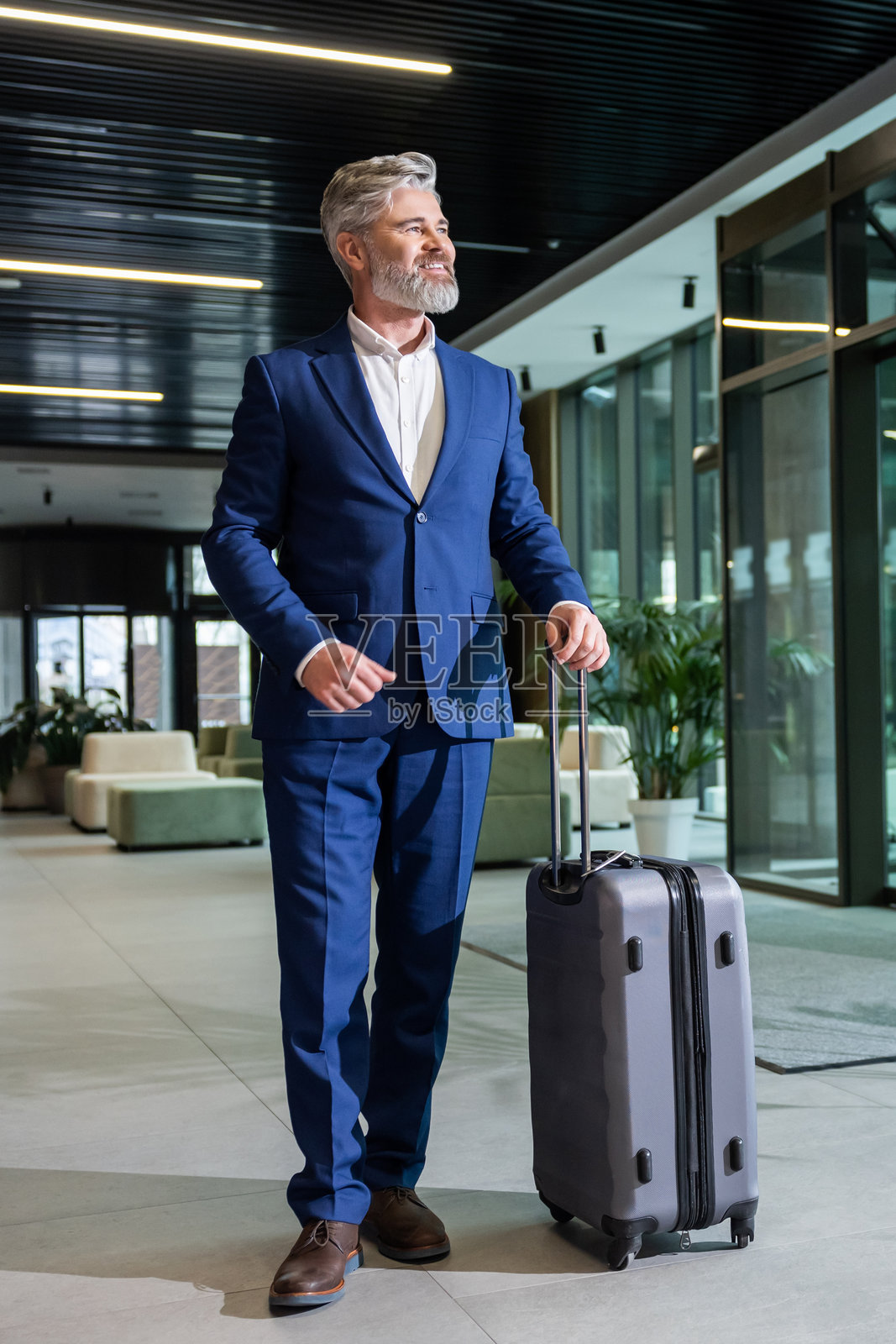 自信的成熟商人手提一个大行李箱,神情坚定照片摄影图片