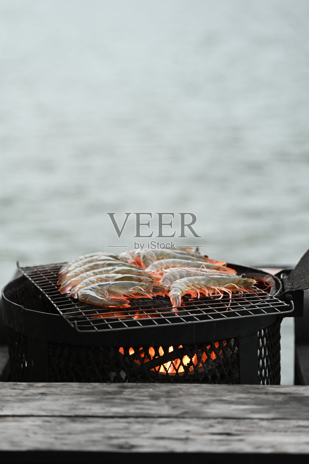 垂直图像:生虾在明火上排列在烤架上,慢慢烹饪至完美,热量将它们的外壳变成鲜艳的橙色,为美味的餐点做好准备。照片摄影图片