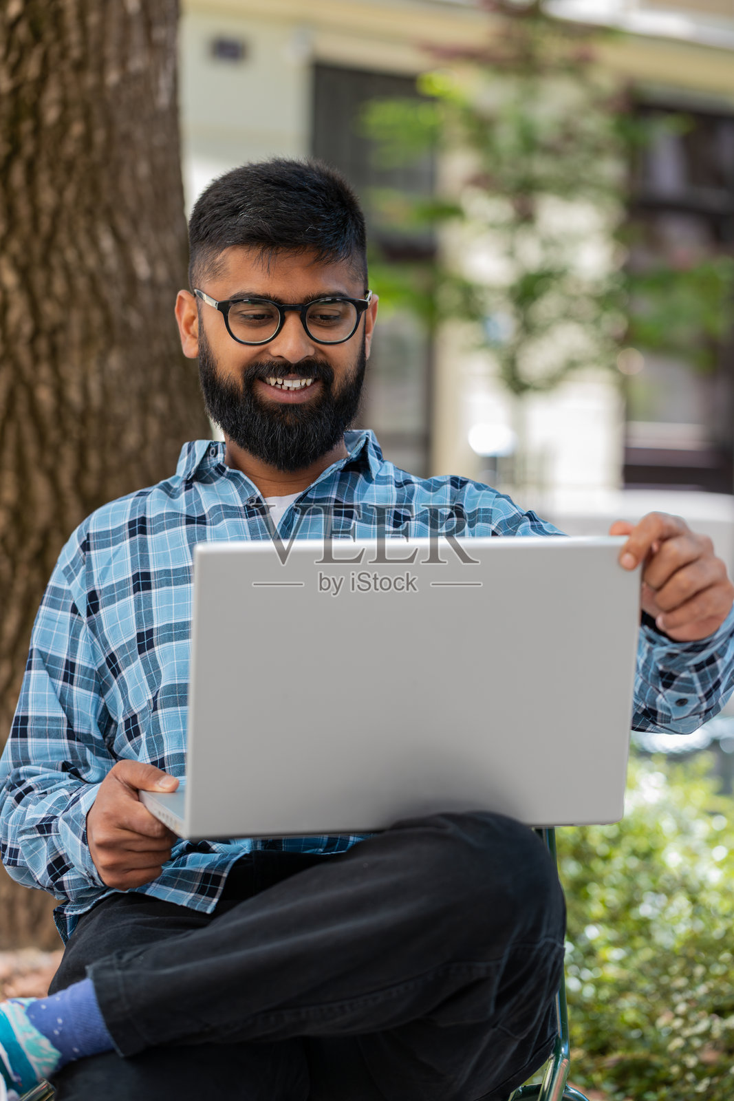 印度男子在城市街道上坐着,使用笔记本电脑远程工作,浏览网站。照片摄影图片