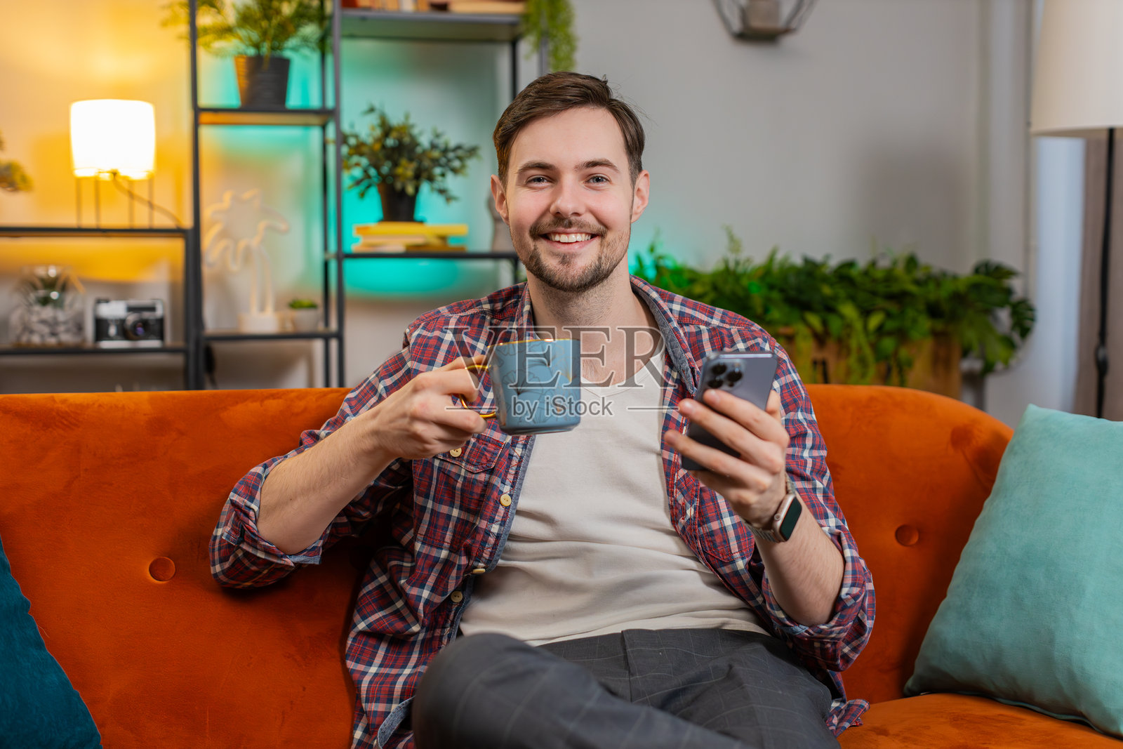 快乐的年轻人一边喝着热咖啡,一边在家用智能手机聊天。照片摄影图片