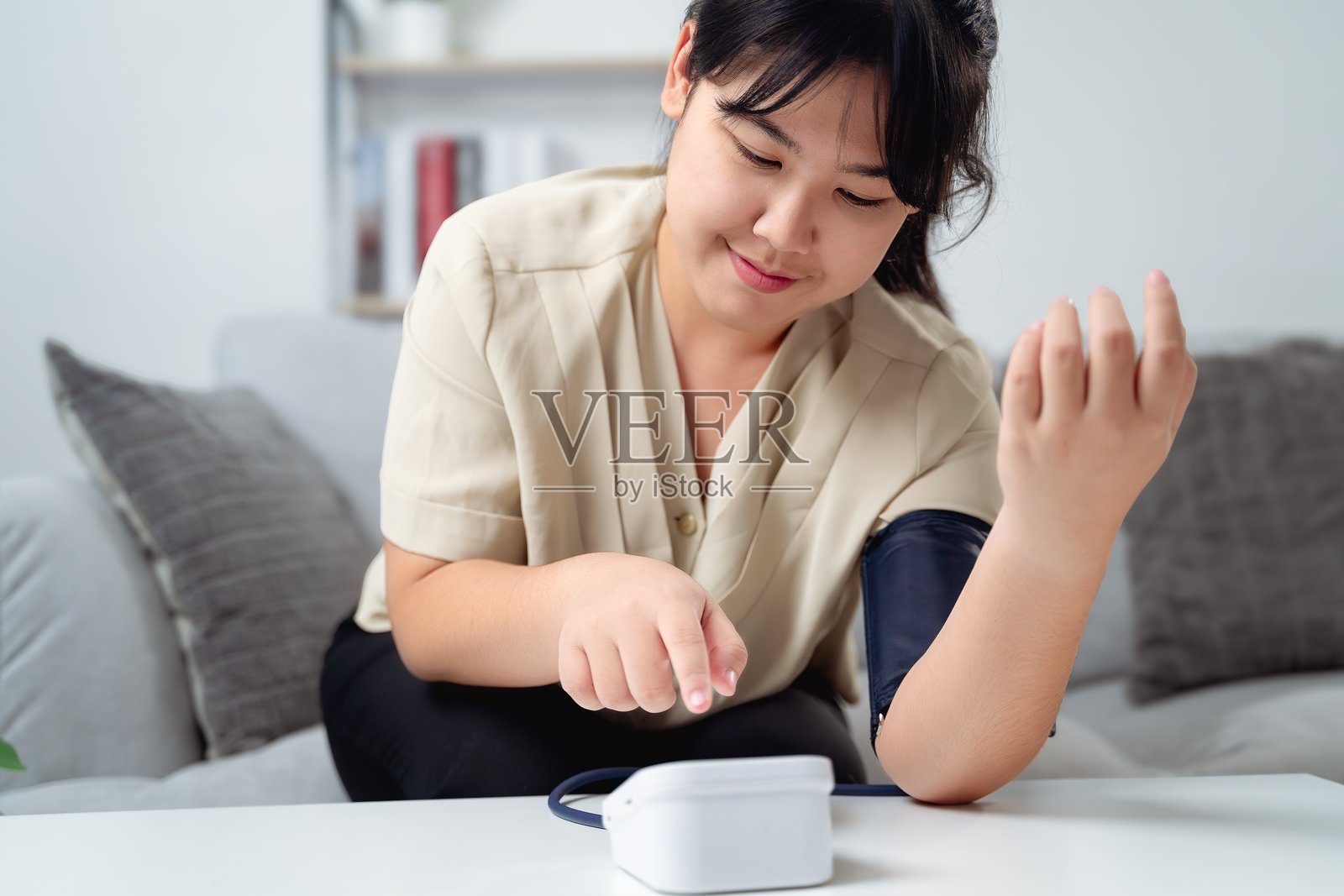 一位女性坐在沙发上,手臂上戴着血压监测仪。她正在测量血压。照片摄影图片