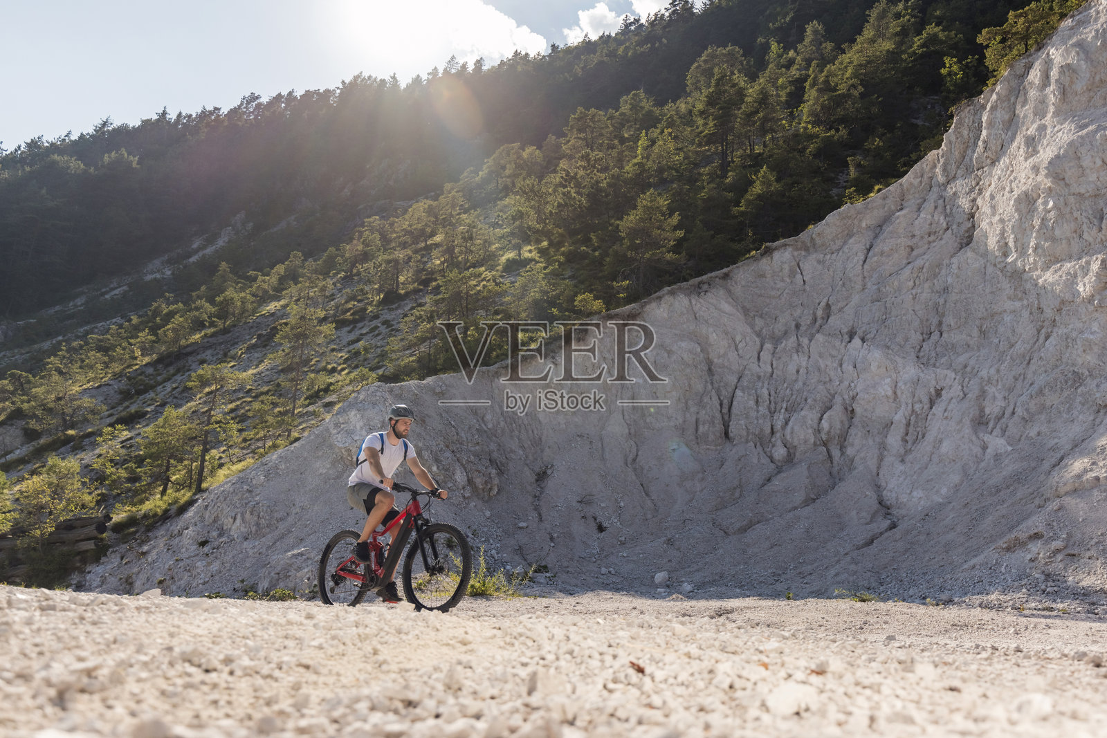 阳光照耀在碎石小径上,一名骑着电动山地车的骑行者。照片摄影图片