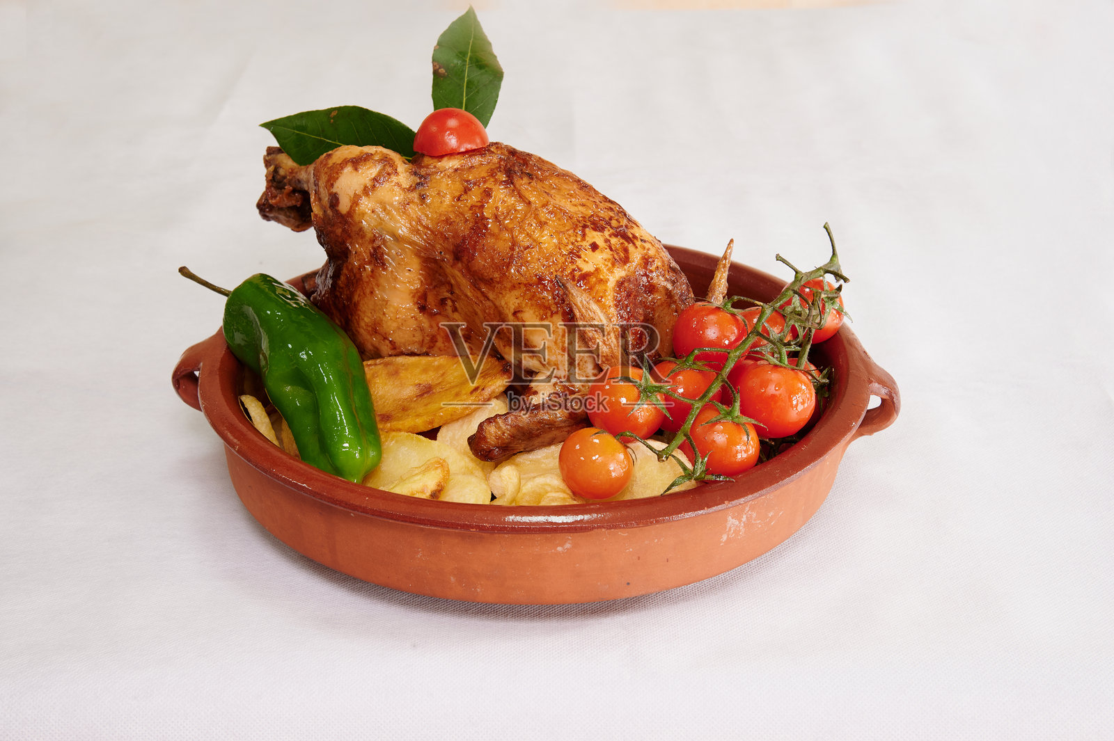 一只鸡坐在盘子上,旁边有一个西红柿和一个辣椒。照片摄影图片