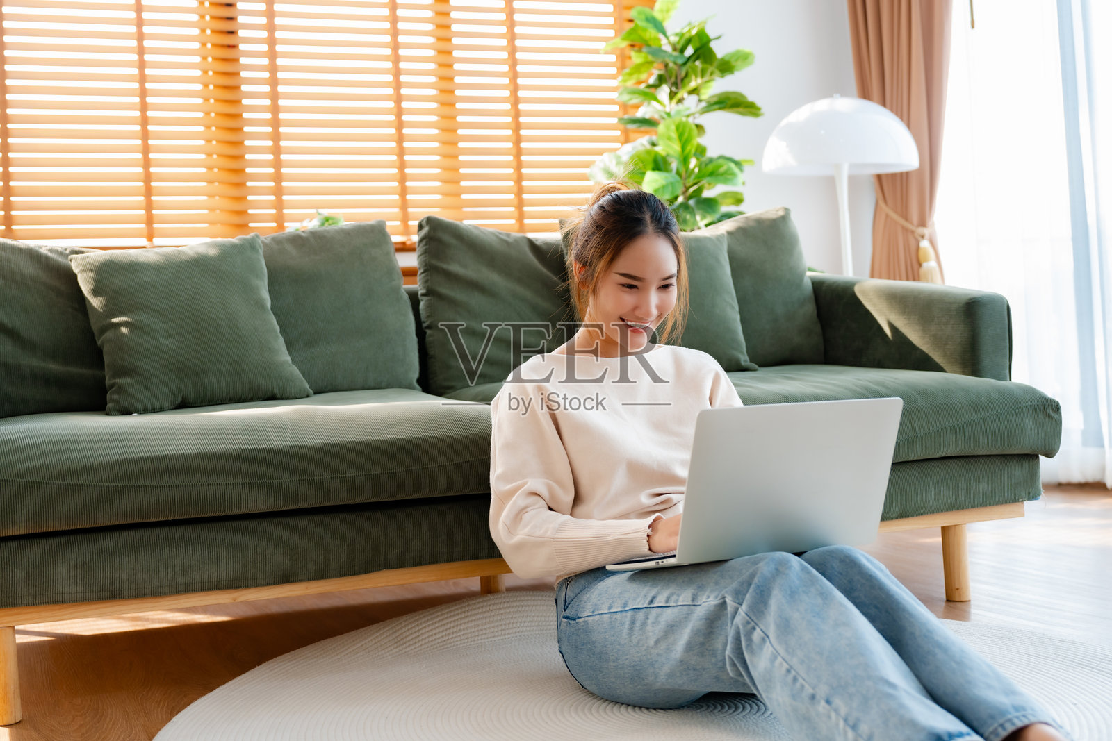 年轻的亚洲美女在舒适的沙发上放松,使用笔记本电脑,快乐的女孩在社交网络上与朋友聊天,度过周末,观看电影,在线购物。照片摄影图片