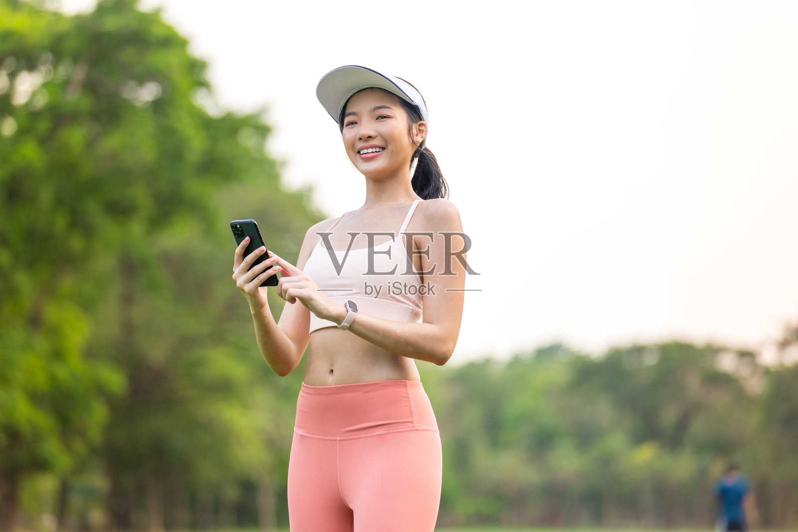 年轻亚洲女性戴着遮阳帽在公园户外锻炼时使用手机照片摄影图片