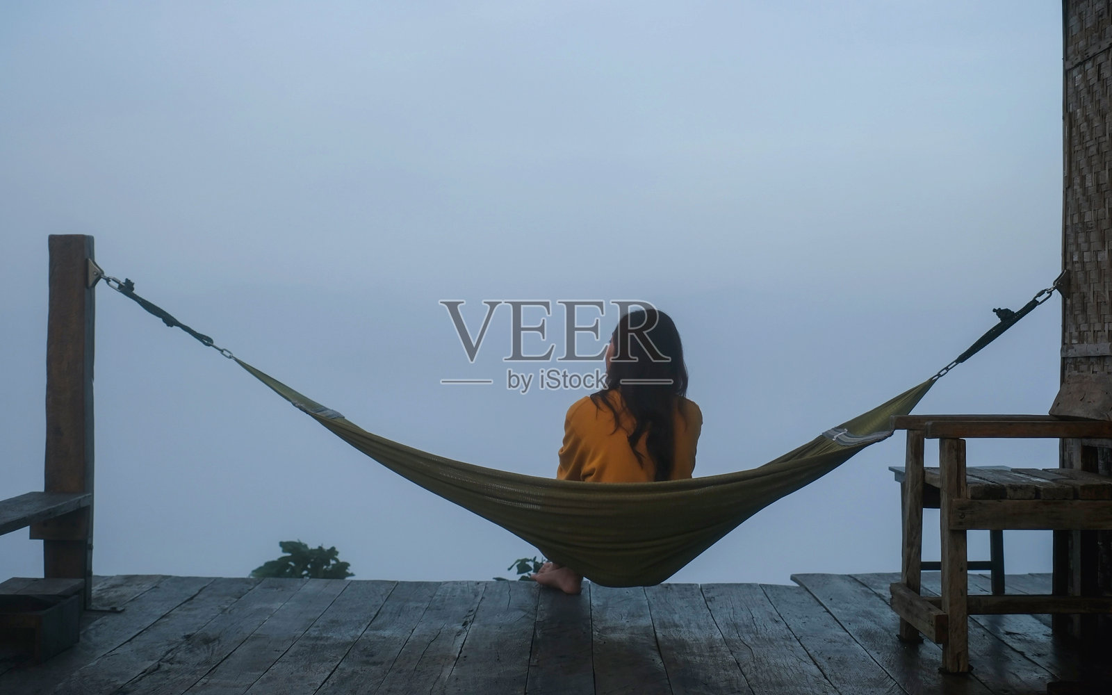 女人坐在吊床上,背对着镜头,欣赏自然风光和雾海。照片摄影图片