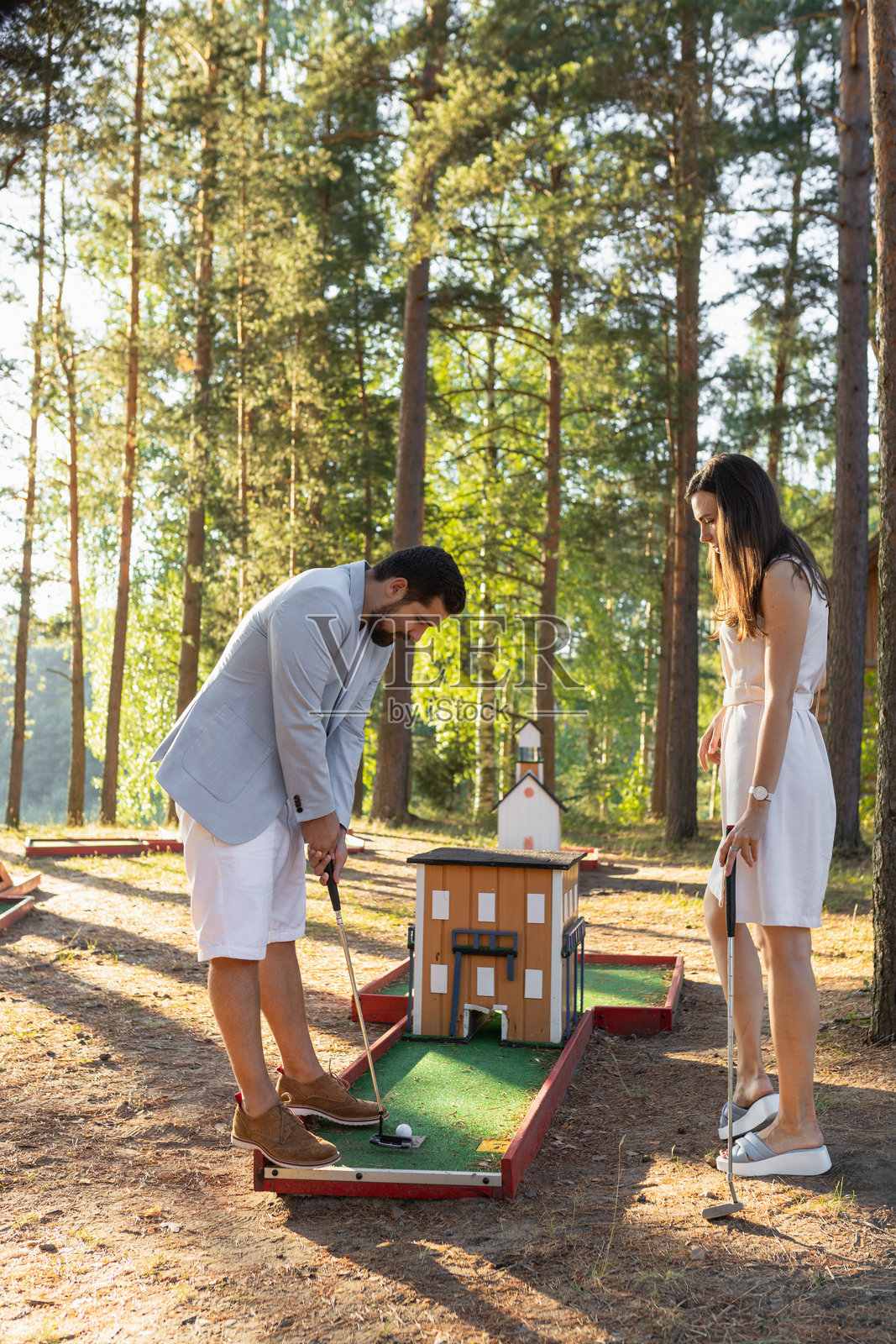 年轻情侣在森林中的户外迷你高尔夫球场玩耍照片摄影图片
