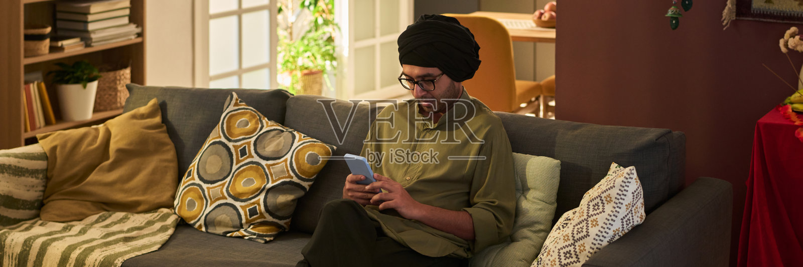 戴着眼镜和头巾的男子坐在沙发上发短信照片摄影图片