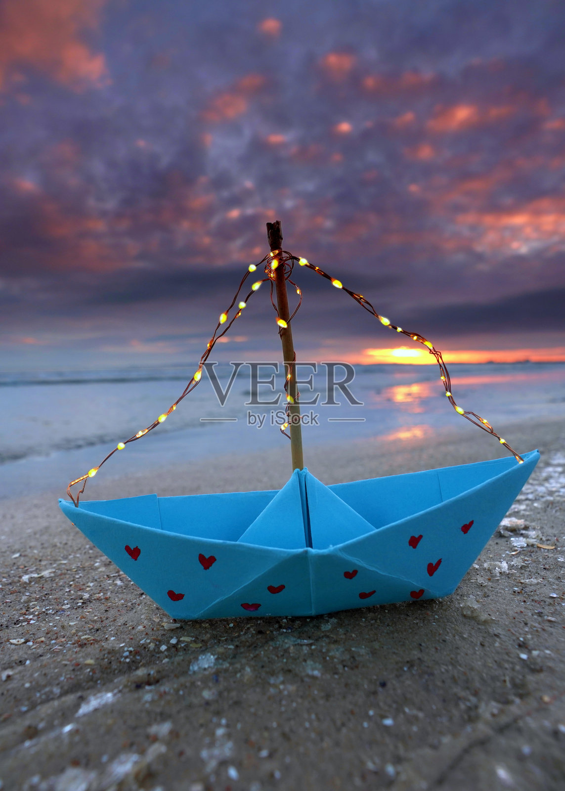 蓝色纸船上有红色心形图案和灯串,停在冰冻的冬季海滩上照片摄影图片