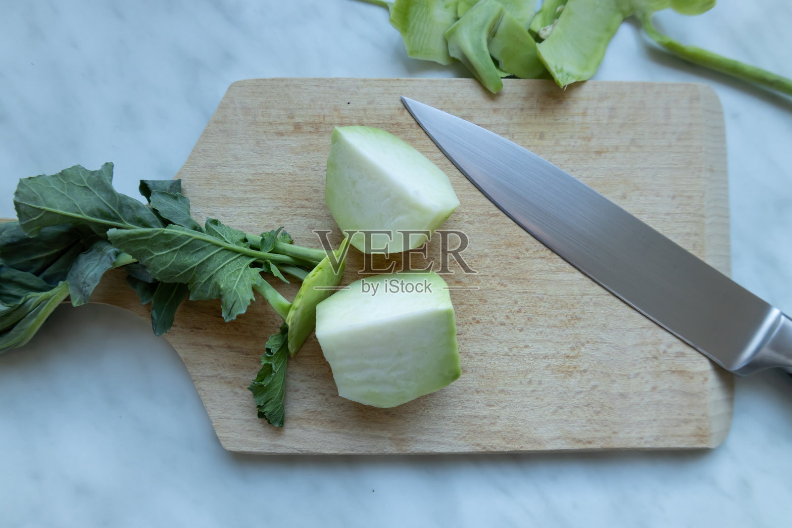切菜板上的新鲜去皮四分之一的甘蓝菜,旁边有一把刀,去掉的外皮清晰可见。照片摄影图片