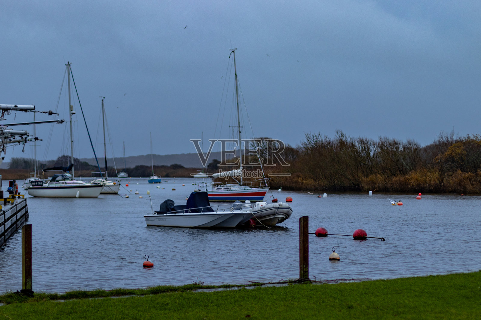 英国基督城码头停泊的宁静船只场景,周围是平静的水面和多云的天空。画面中展现了帆船和摩托艇。照片摄影图片