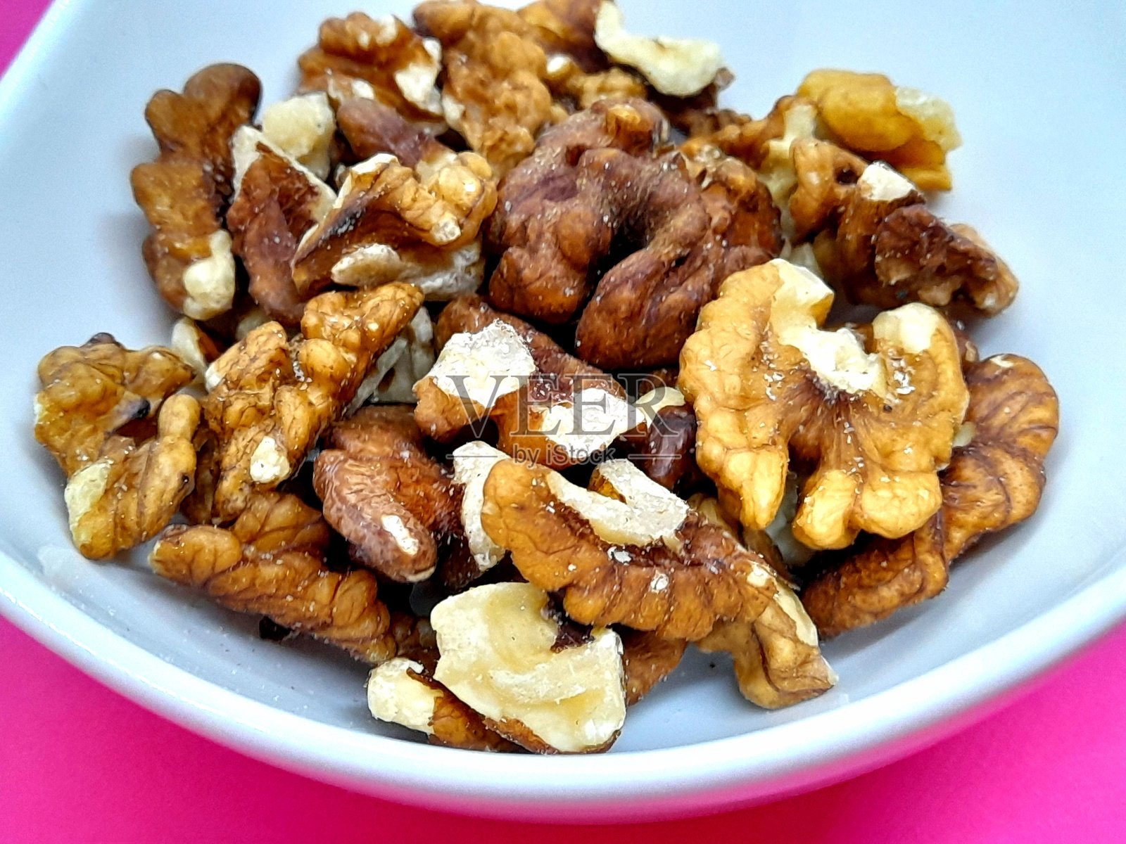 小碗里的核桃和粉色背景。照片摄影图片
