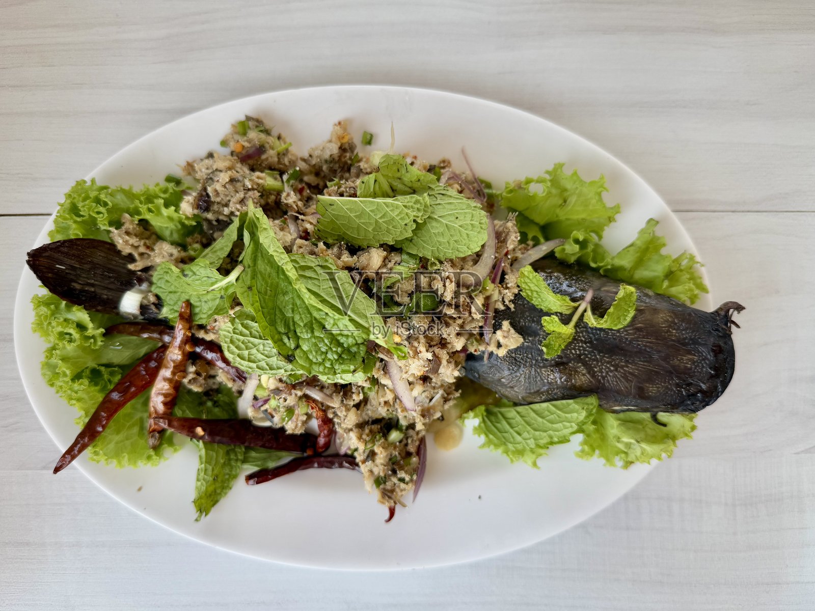 白盘上的泰式香辣剁碎鱼沙拉,放在木桌上照片摄影图片