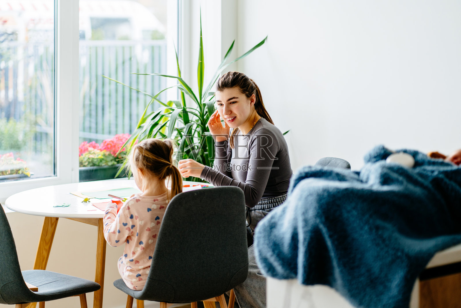 年轻母亲和她四岁的女儿坐在窗边明亮的桌子旁,享受创意时光。她们一起聊天、剪裁、上色,制作心形主题的手工艺品。照片摄影图片