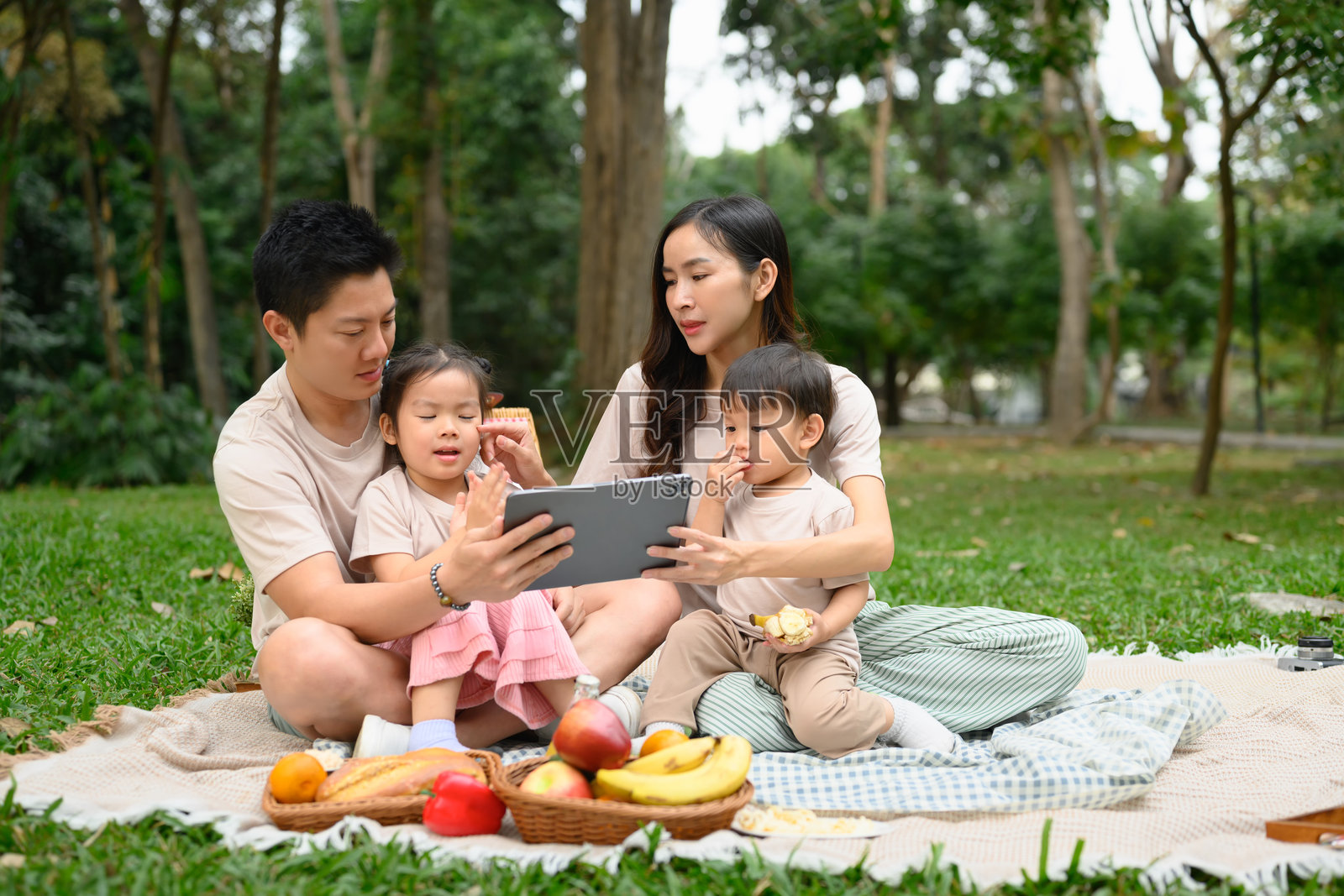 快乐的家庭在公园野餐时观看数字平板上的内容照片摄影图片
