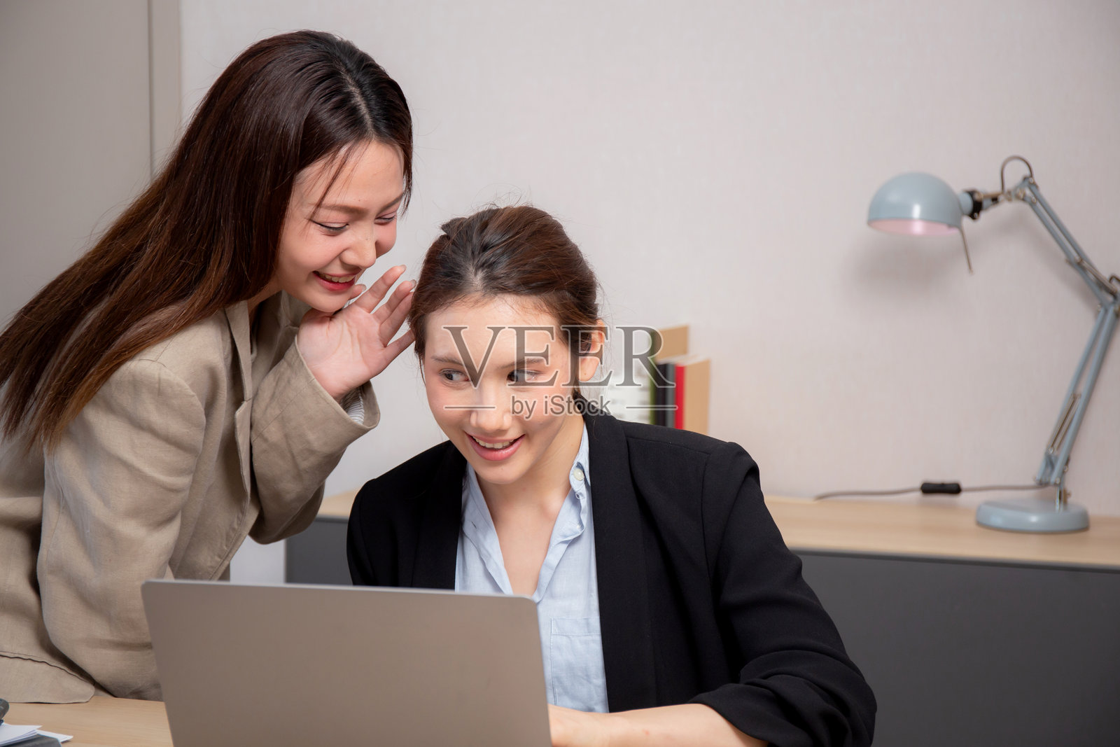 两位女商人在现代办公室里低声私语,分享八卦,进行互动。照片摄影图片