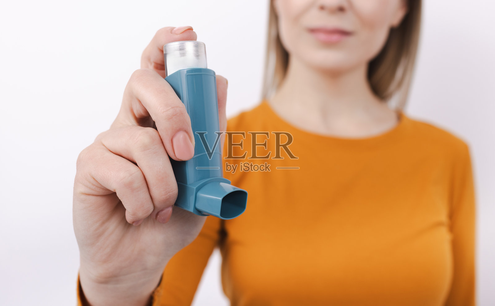 女性在室内白色背景下手持便携式哮喘吸入器。哮喘治疗照片摄影图片